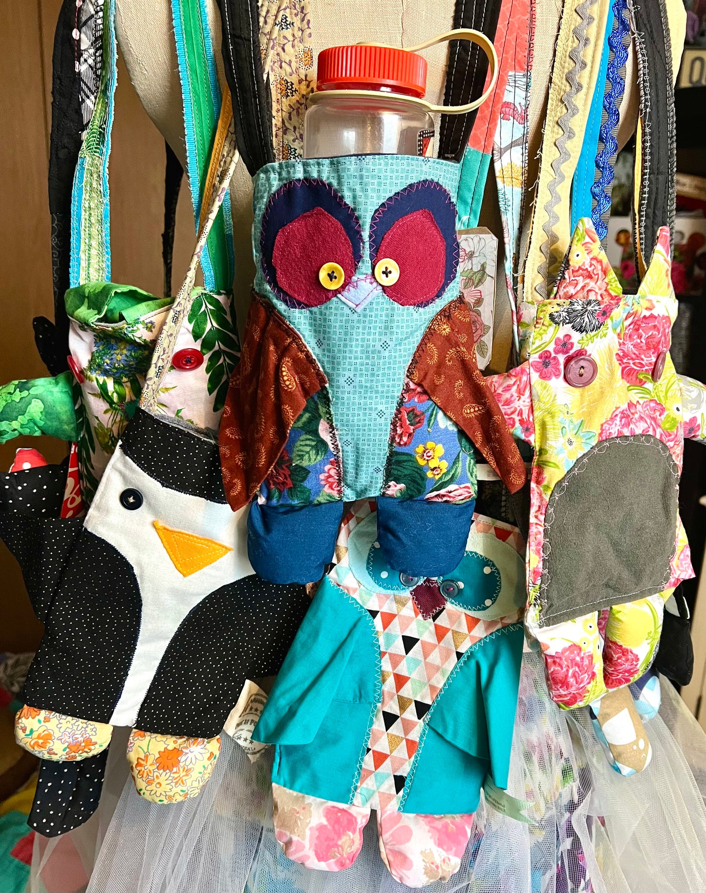 Colorful fabric owl with a water bottle on a mannequin with a floral dress.