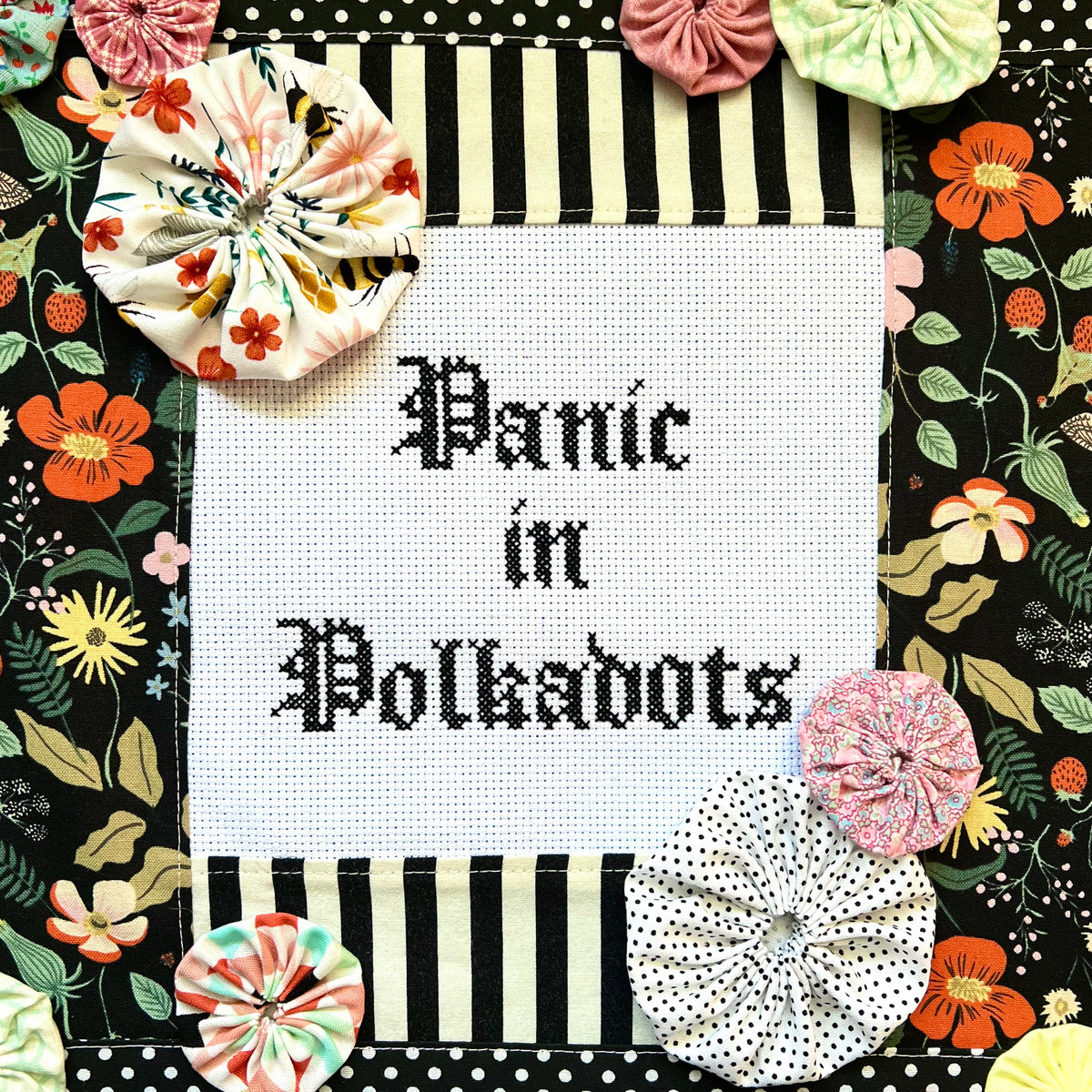 Decorative frame with floral, yoyos, and polka dot patterns and cross-stitched text 'Panic in Polkadots'.