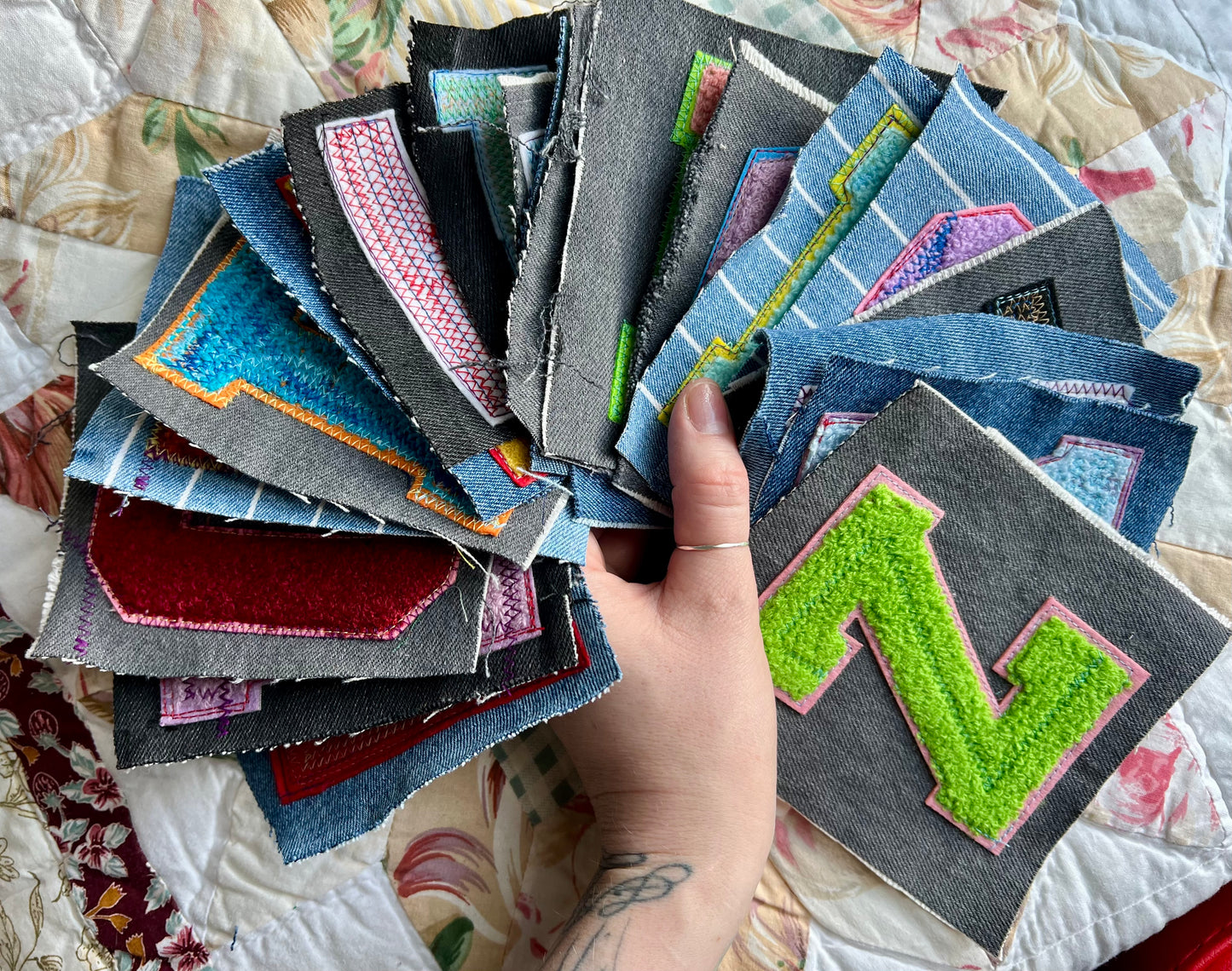 Hand holding a variety of colorful fabric letter patches on a quilty background