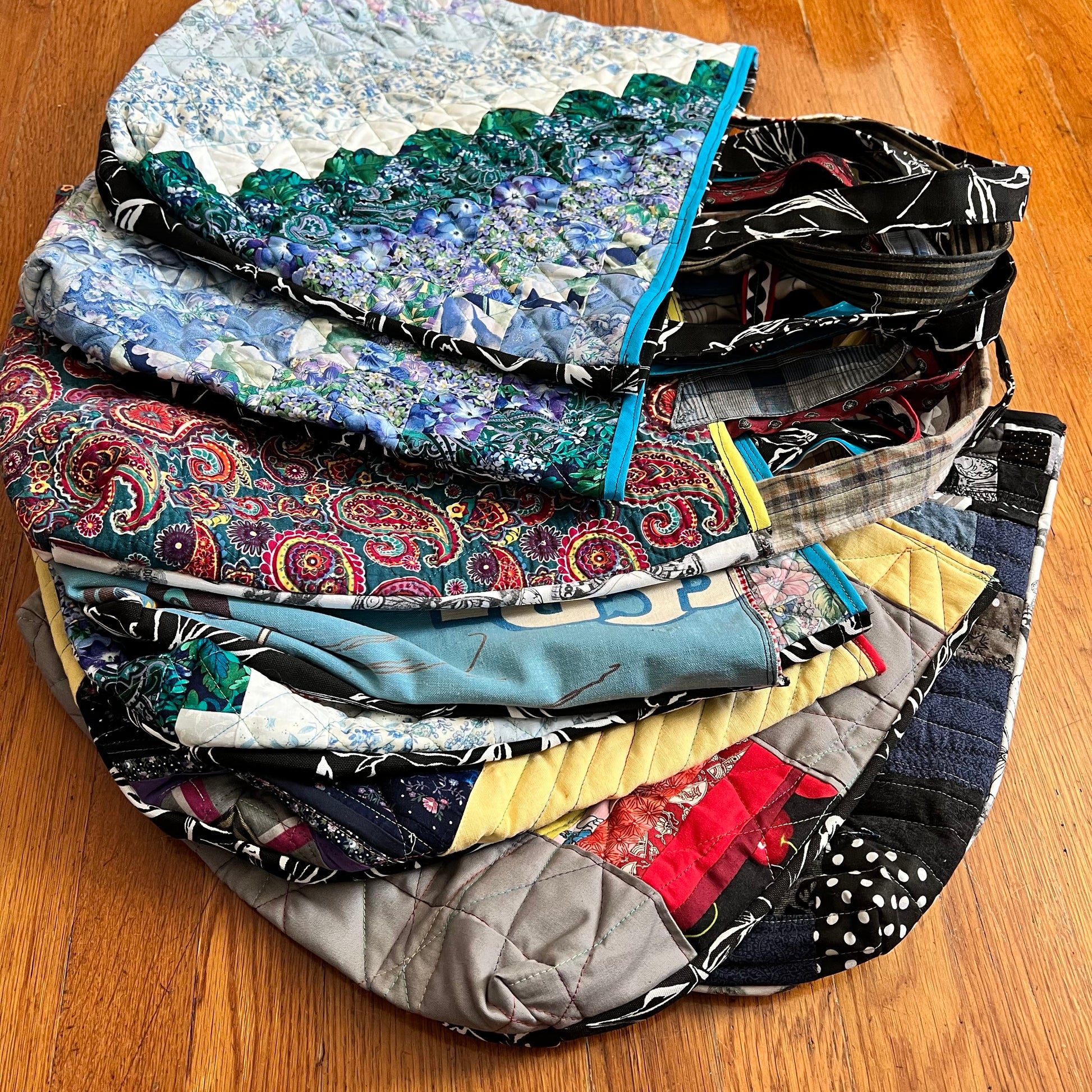 A stack of perfectly imperfect tote bags, laid out on a wood floor.