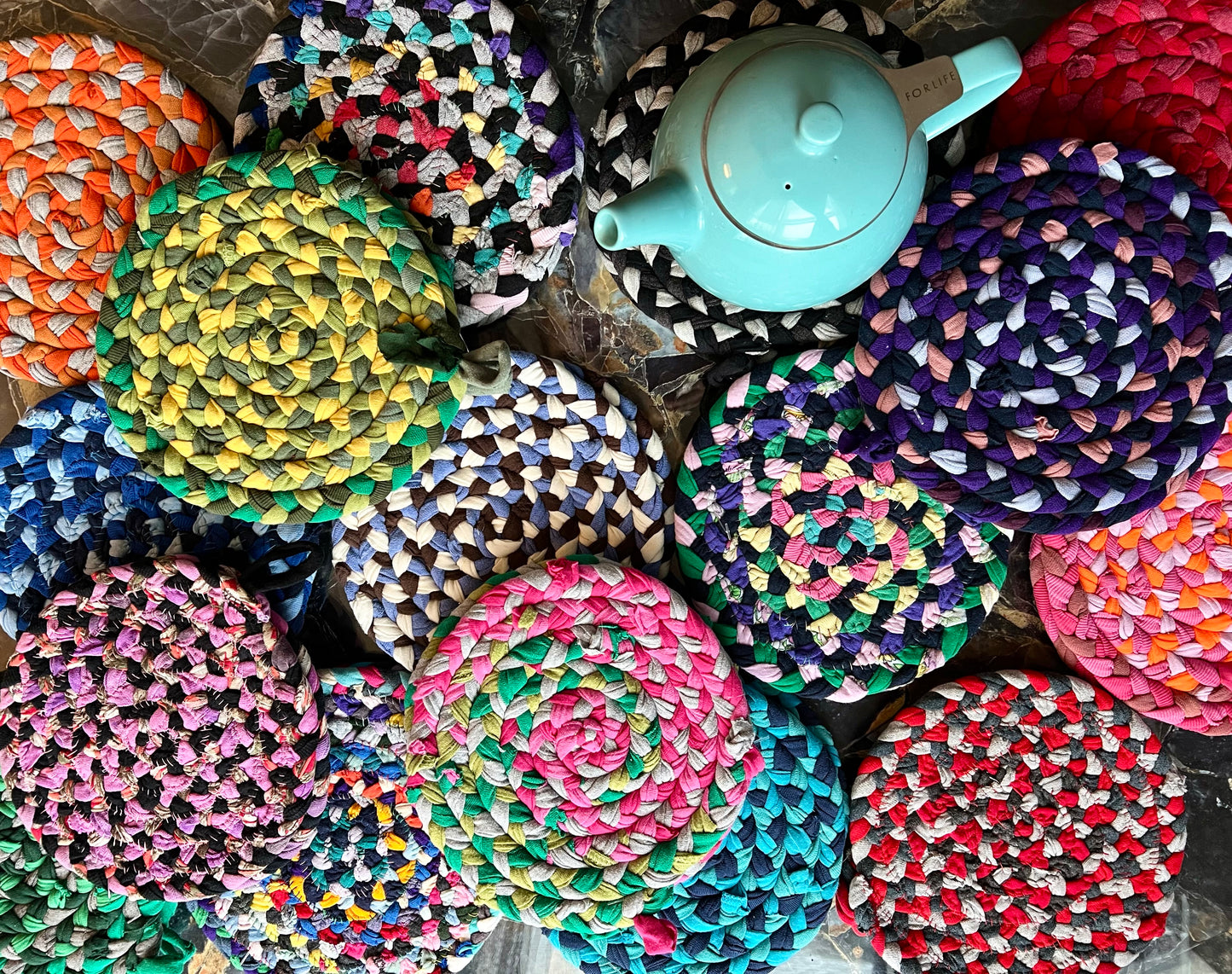 Colorful braided potholders with a turquoise teapot on top of one of them, aerial view.