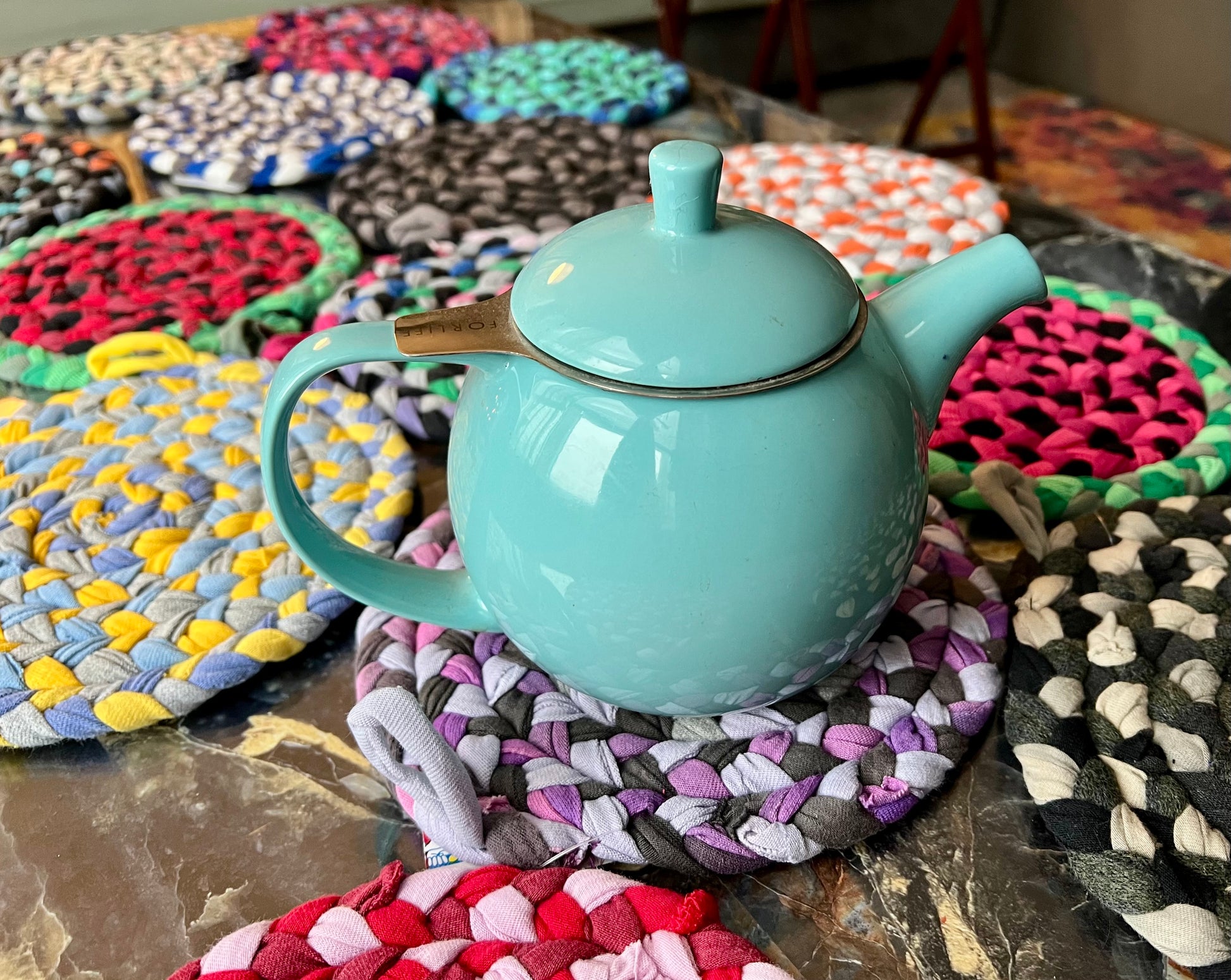 Turquoise teapot on colorful braided trivet potholders