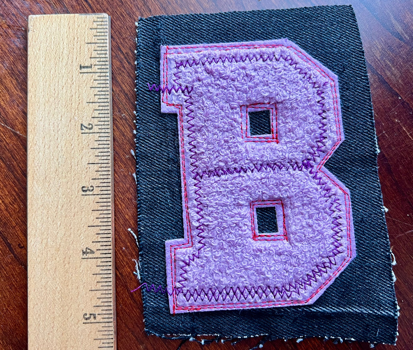 Patch with letter 'B' on a dark fabric background, next to a ruler for scale.