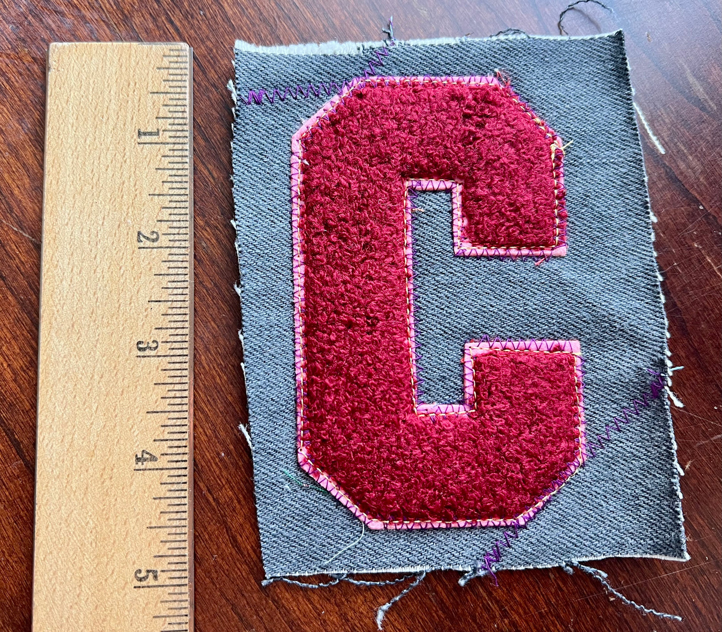 Fabric patch with a red 'C' letter on gray fabric next to a ruler for scale.
