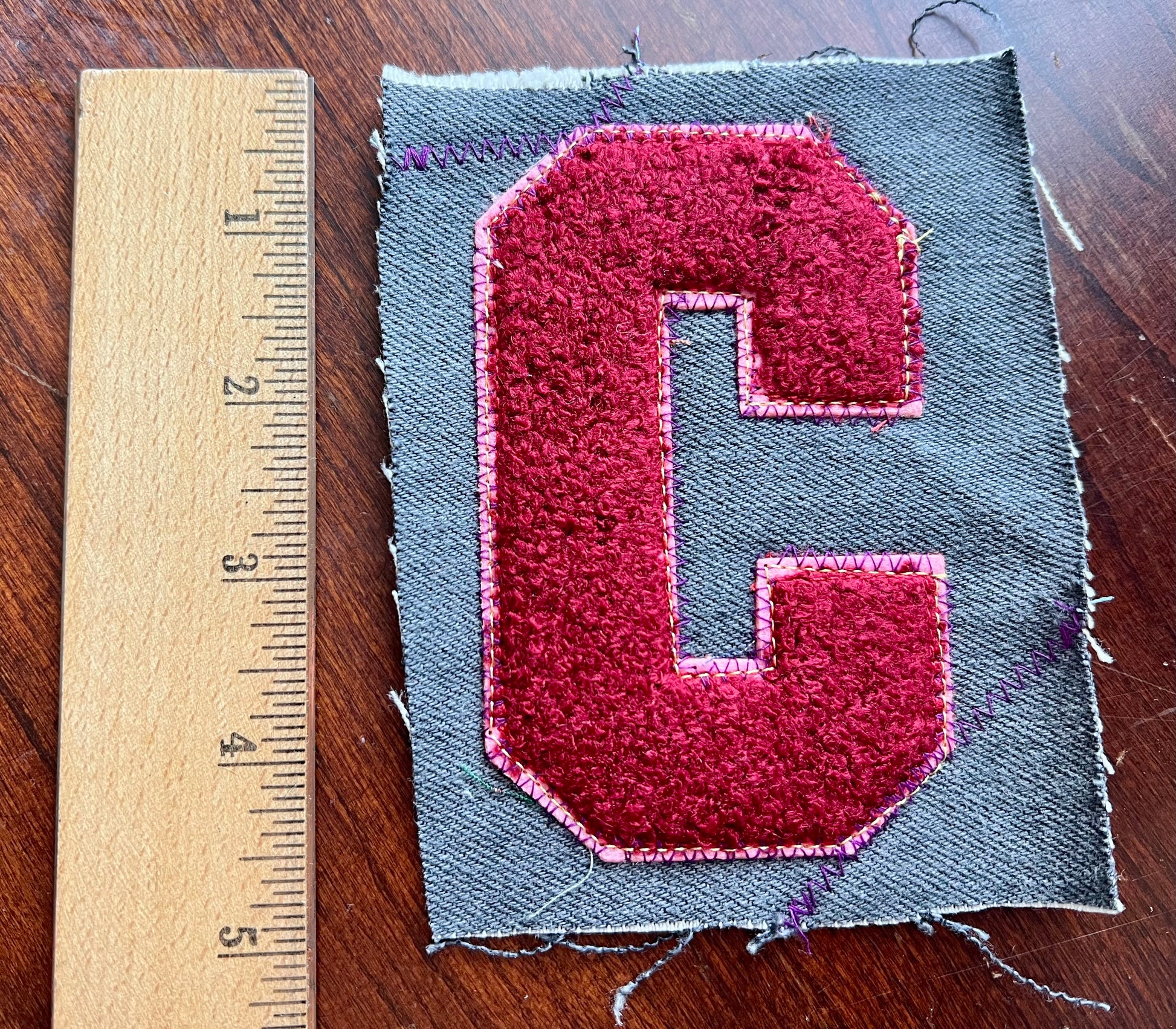 Fabric patch with a red 'C' letter on gray fabric next to a ruler for scale.