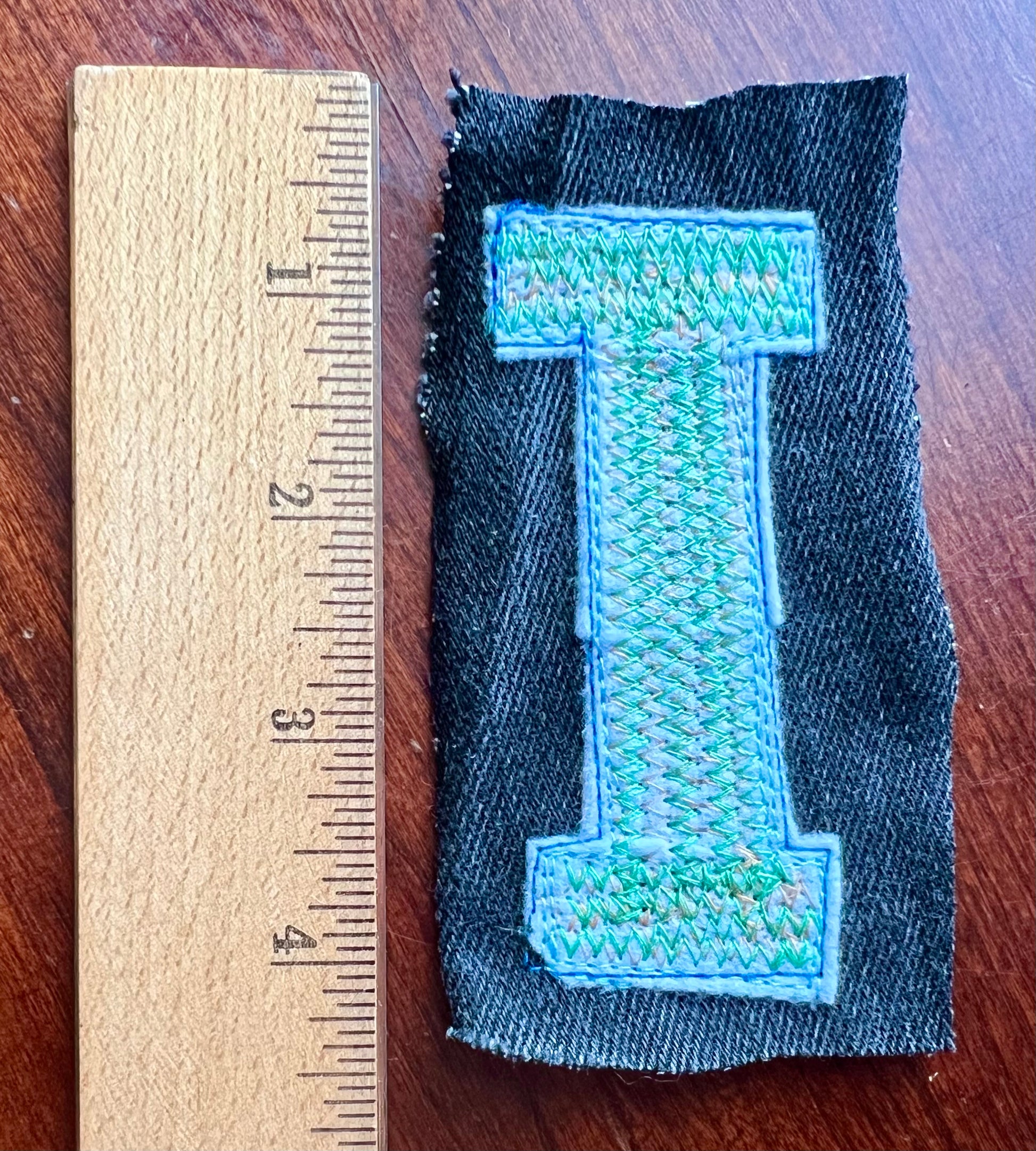 Fabric patch with letter’I' next to a ruler on a wooden surface