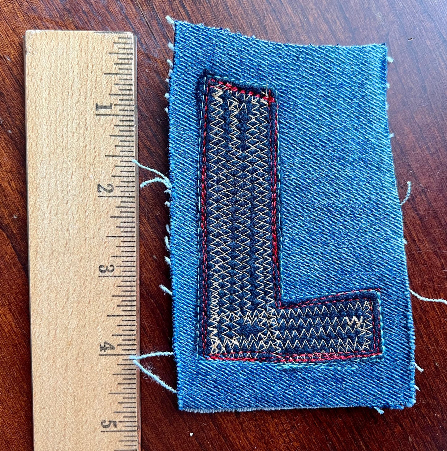 Blue denim patch with woven pattern next to a wooden ruler on a wooden surface