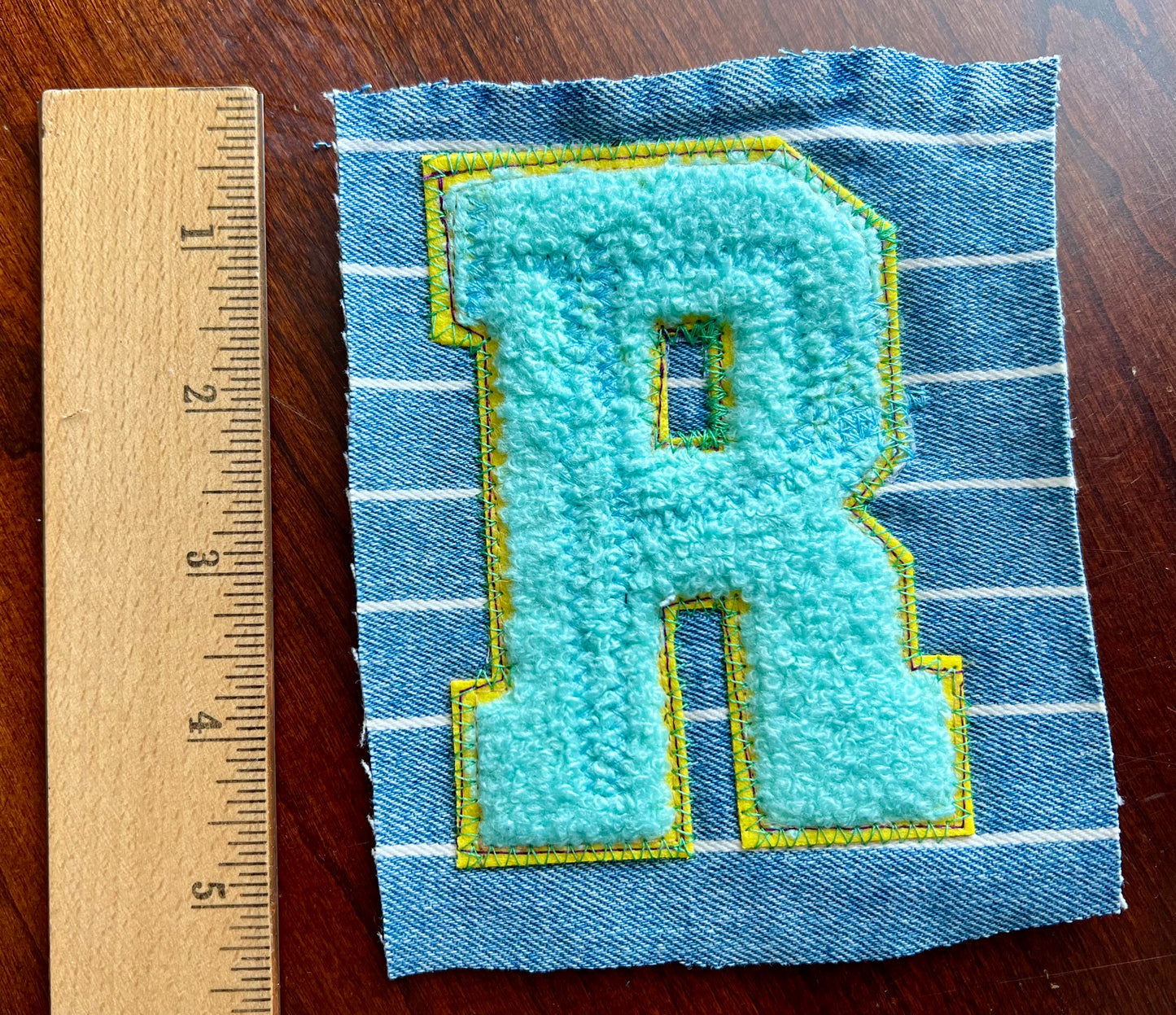 Fabric patch with letter 'R' on a wooden ruler for scale