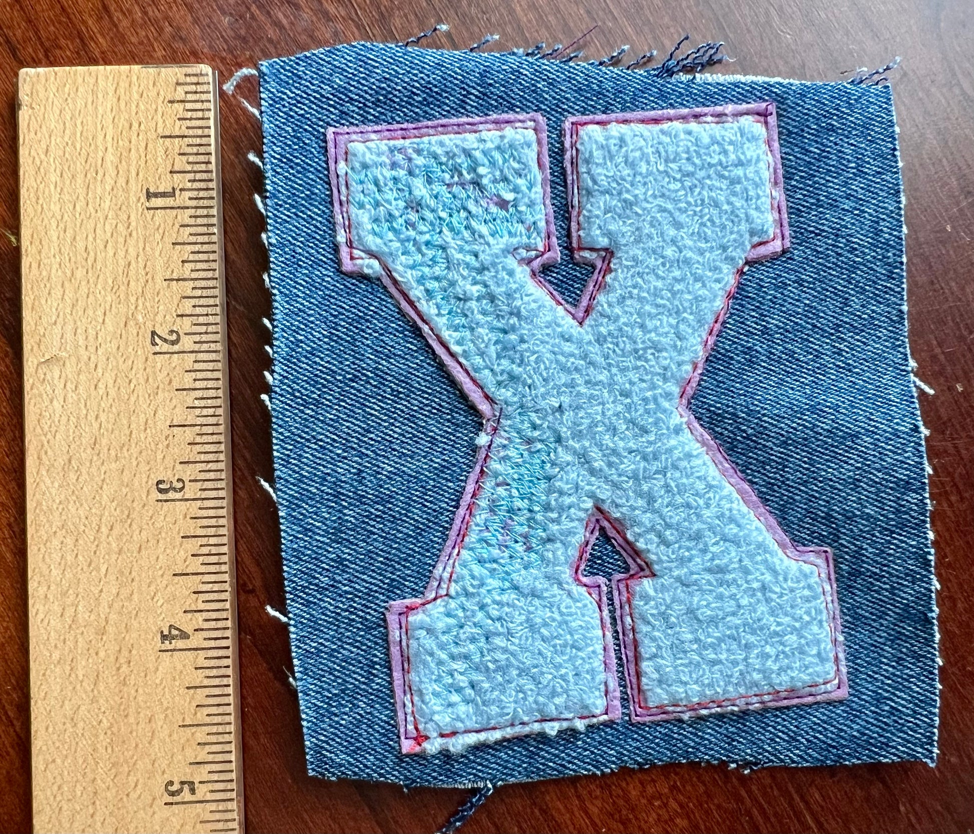 Denim patch with a letter 'K' design next to a wooden ruler on a wooden surface