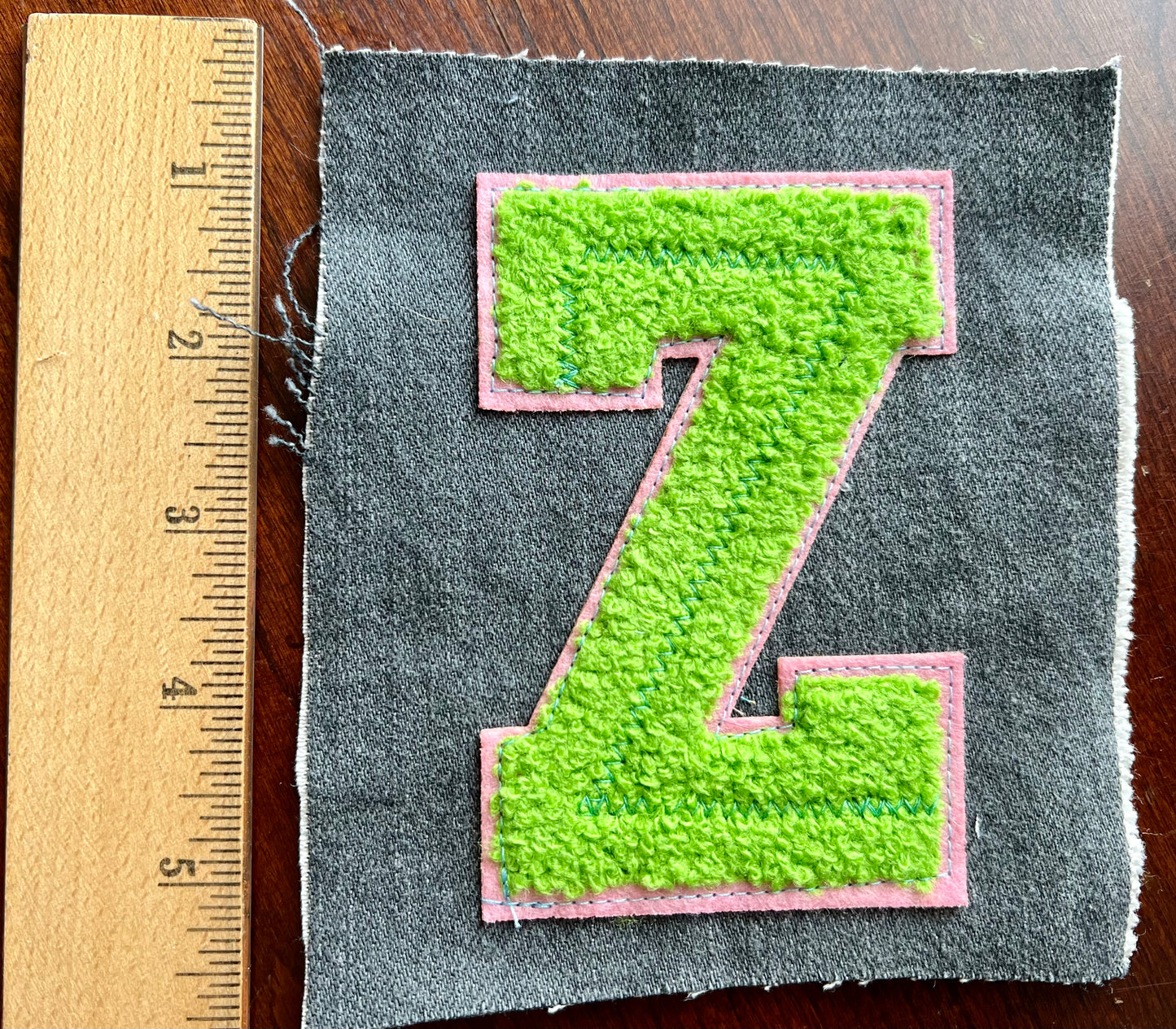 Green letter 'Z' patch on gray fabric with a wooden ruler for scale.