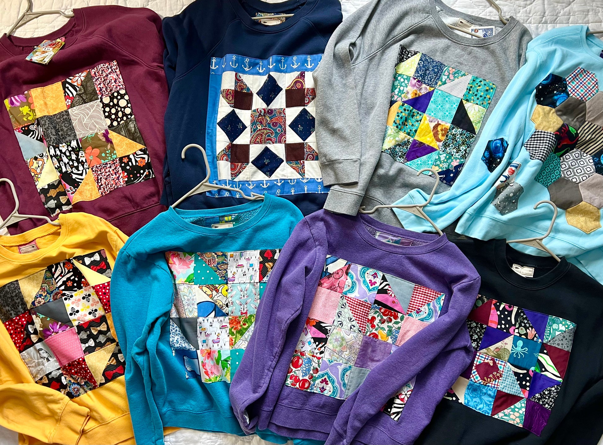 Collection of colorful sweatshirts with patchwork designs on a textured surface.