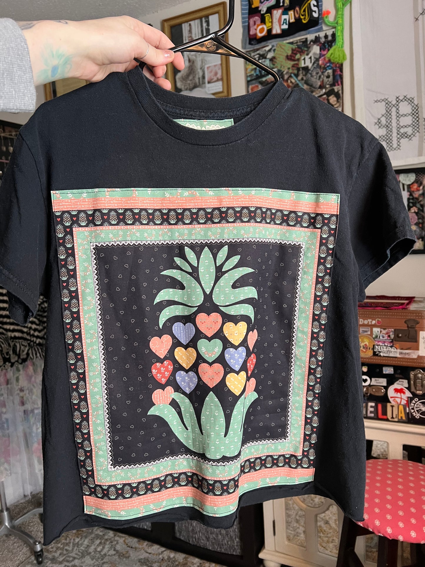Black shirt with colorful floral design held by a person in a casual setting.
