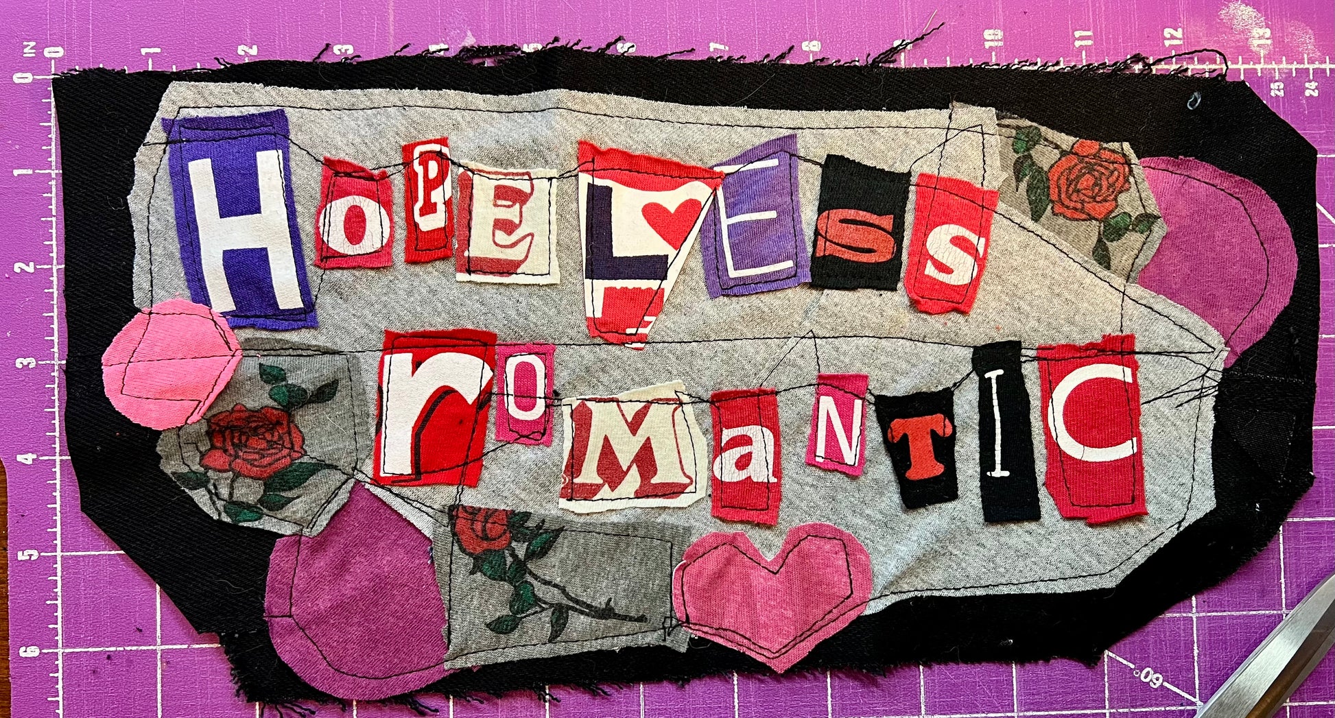 Textual art piece with fabric letters spelling 'HOPELESS ROMANTIC' on a purple background.