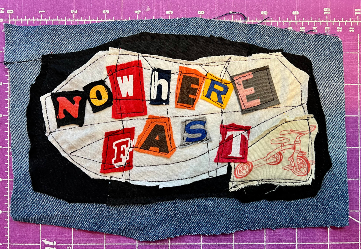 Textile art piece with 'NOWHERE FAST' on a purple grid background