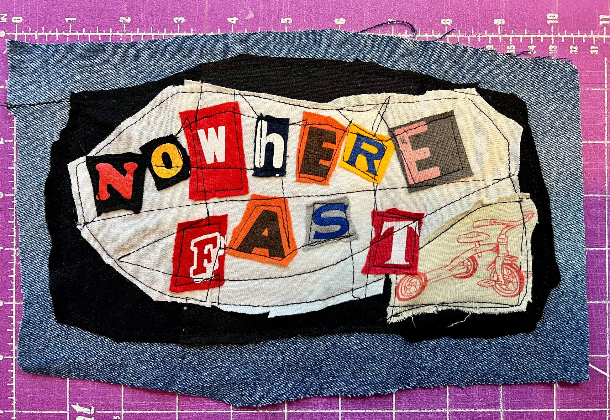 Textile art piece with 'NOWHERE FAST' on a purple grid background