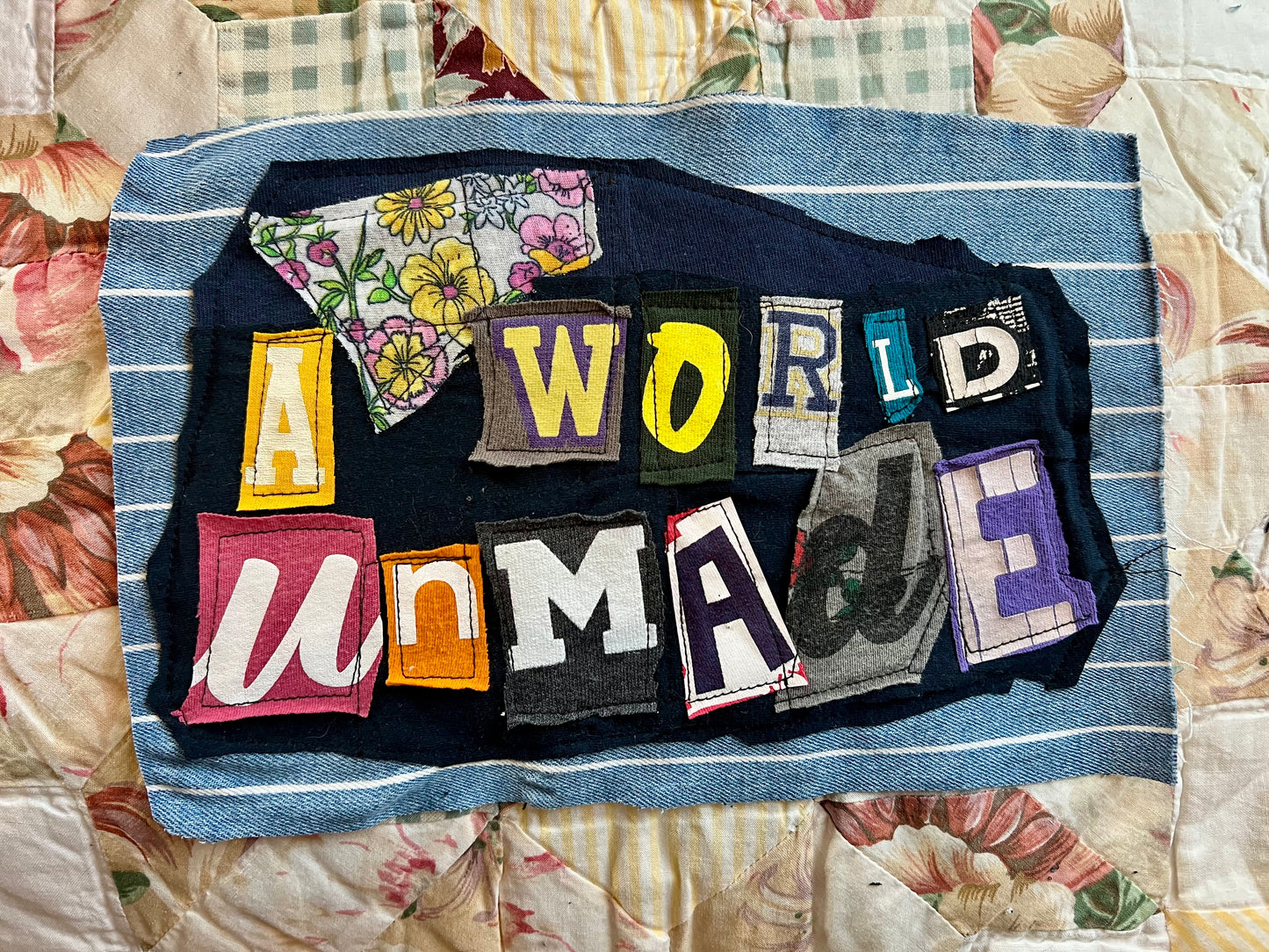 Textile art piece with colorful letters spelling 'A World Unmade' on a floral background