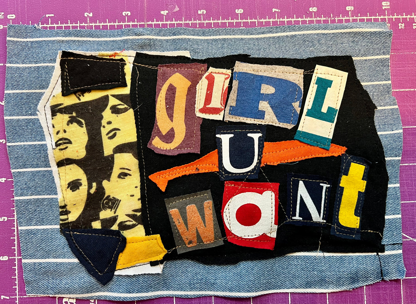 Collage of fabric with cut-out letters spelling 'GIRL U WANT' on a purple cutting mat.