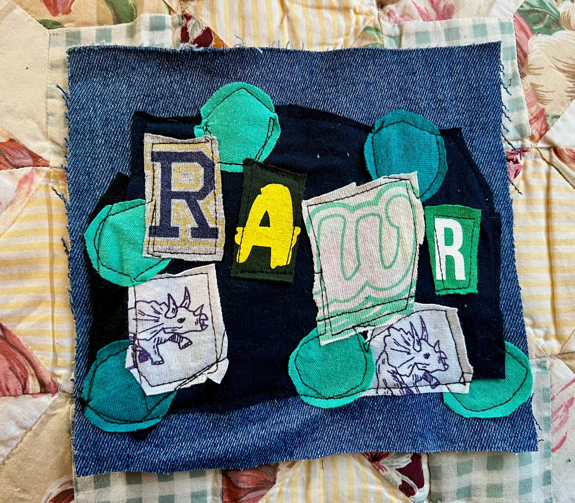 Textile art piece with fabric letters spelling 'RAWR' on a patchwork background