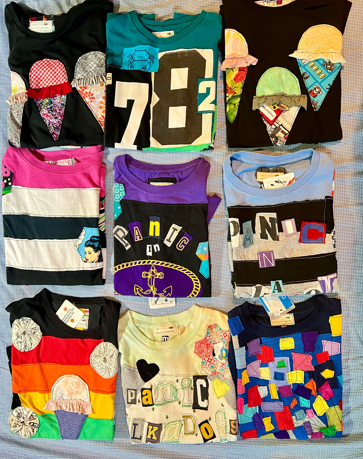 Nine folded graphic t-shirts arranged in a 3x3 grid on a light blue textured fabric background. The shirts feature various colorful designs, including ice cream cone graphics, bold numbers, and patchwork patterns.