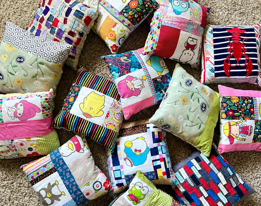A collection of colorful handmade patchwork pillows with various cartoon and floral prints, arranged on a beige carpet.