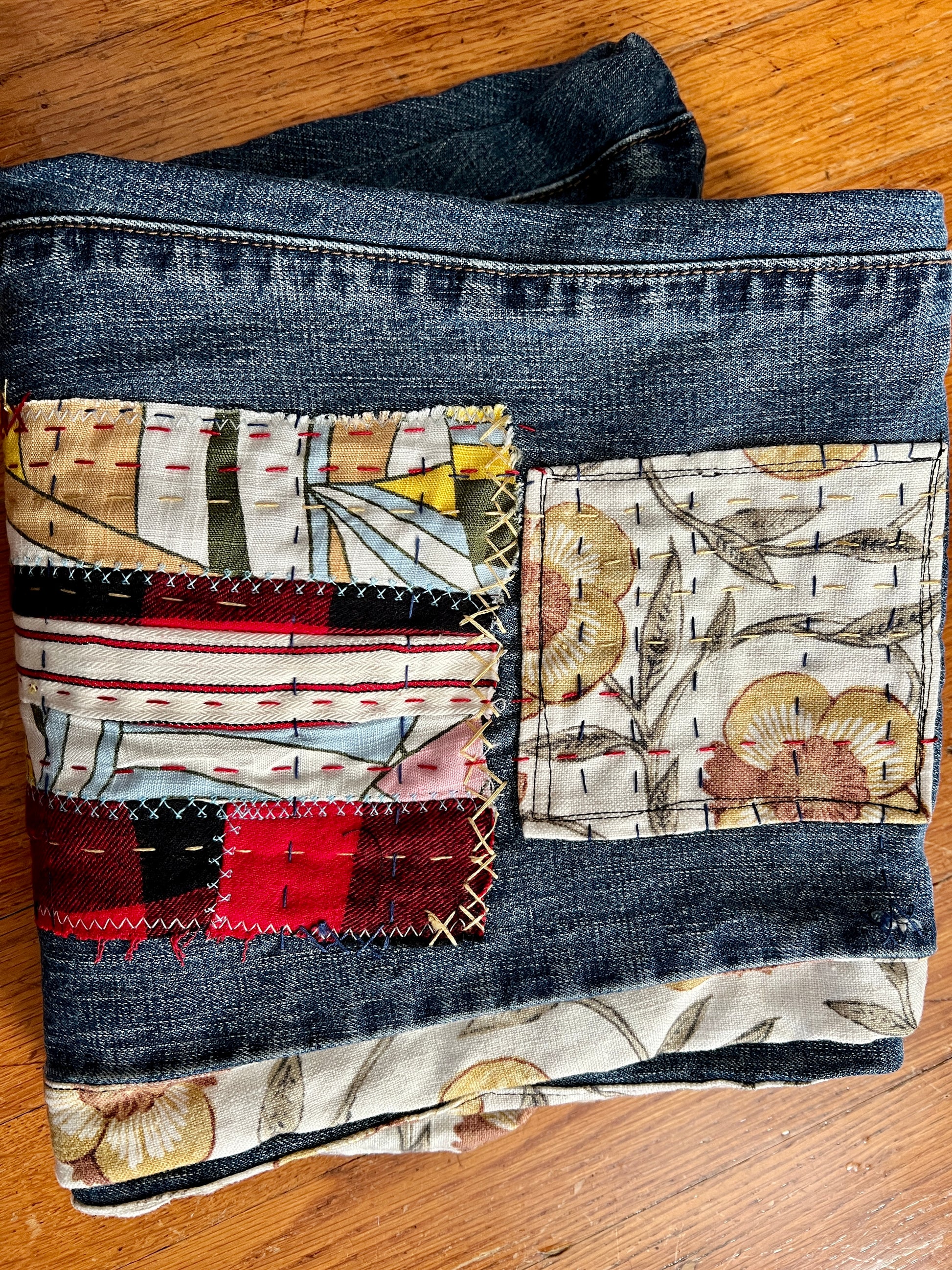 Patchwork fabric with floral and abstract patterns sewn onto a pair of jeans on a wooden surface