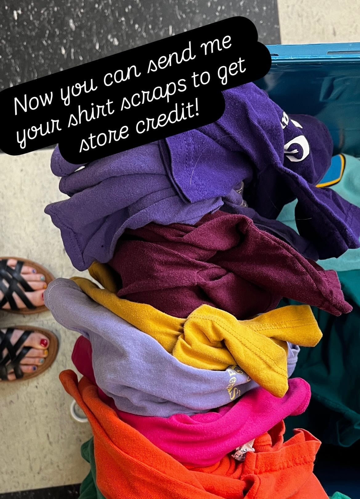 A pile of colorful folded fabric scraps in purple, burgundy, lavender, yellow, pink, and orange next to a blue suitcase, with a black text overlay that reads 'Now you can send me your shirt scraps to get store credit!'.