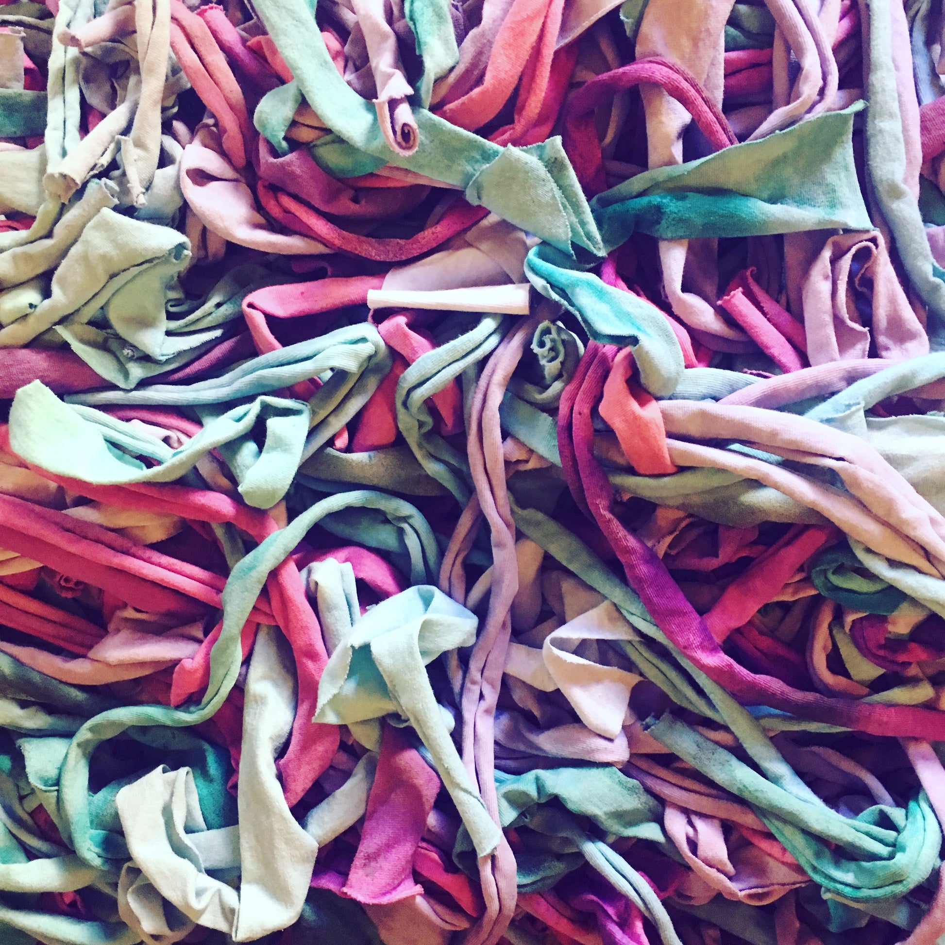 A close-up pile of colorful, multi-colored fabric tshirt strips  in shades of pink, green, red, and beige.