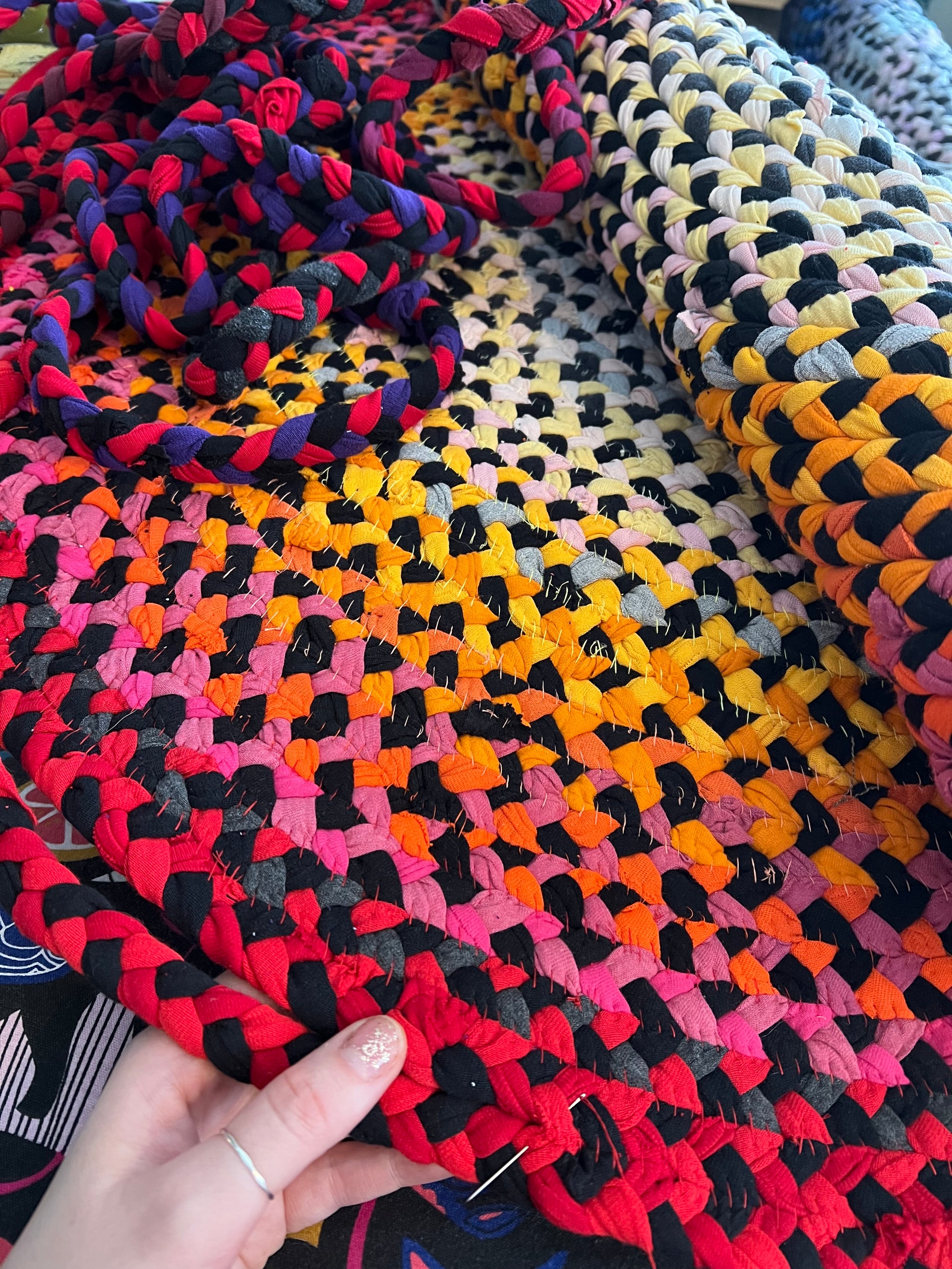 Colorful braided rug with a hand holding the edge, as a work in progress.