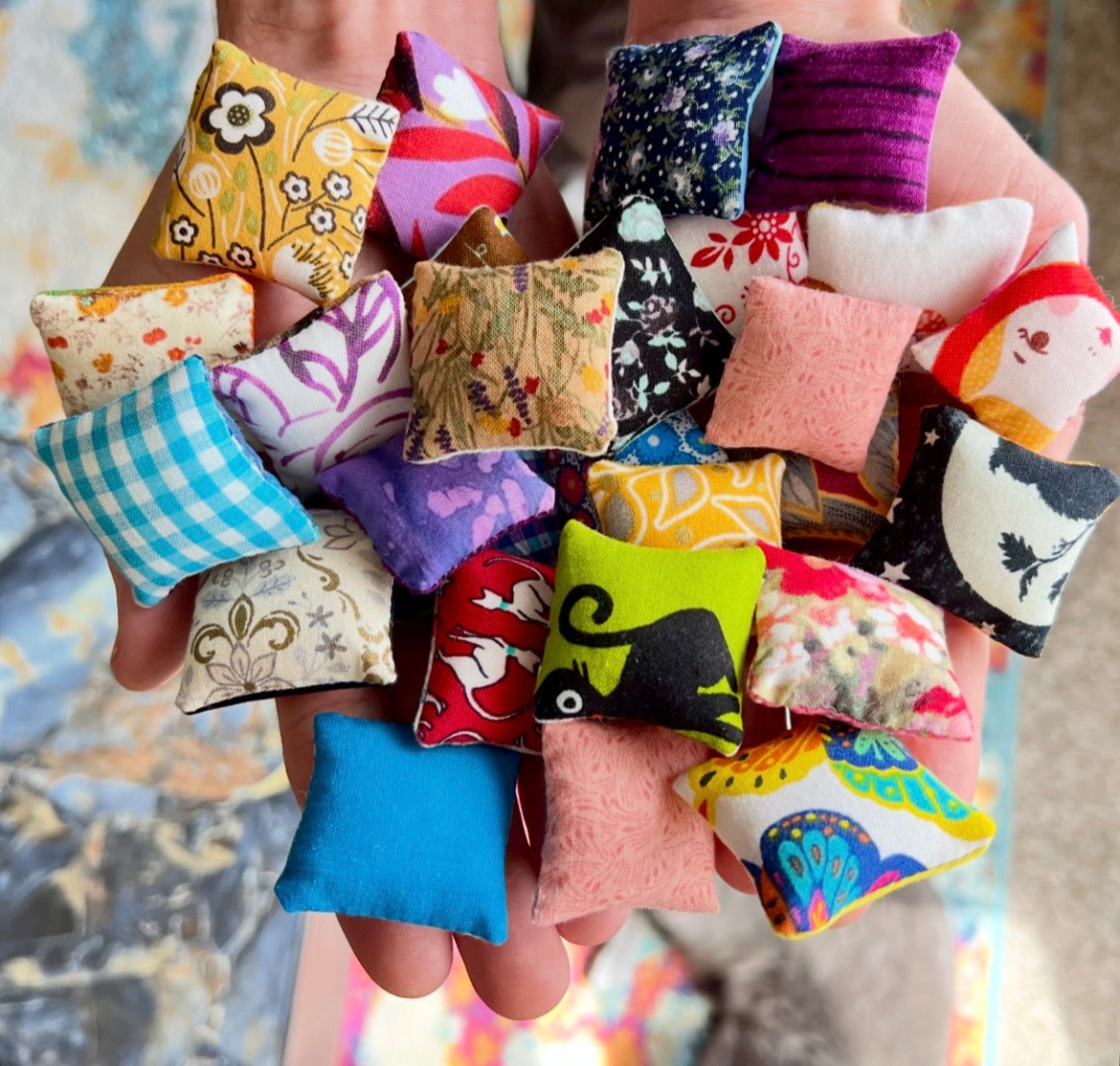 Hand holding a collection of colorful fabric pillows with various patterns, held in hands for scale