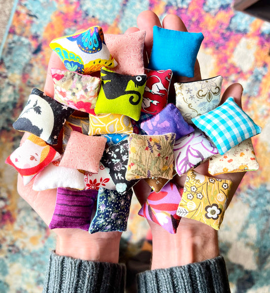 Hand holding a collection of colorful fabric pillows with various patterns, held in hands for scale