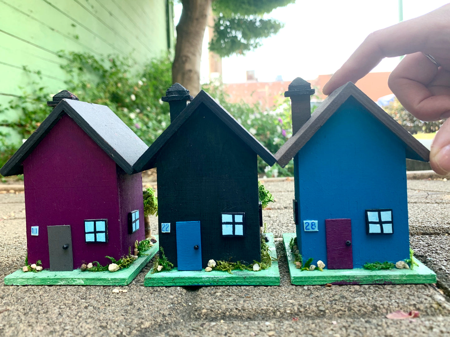 A row of tiny dollhouses, front view, and a hand holds one of them
