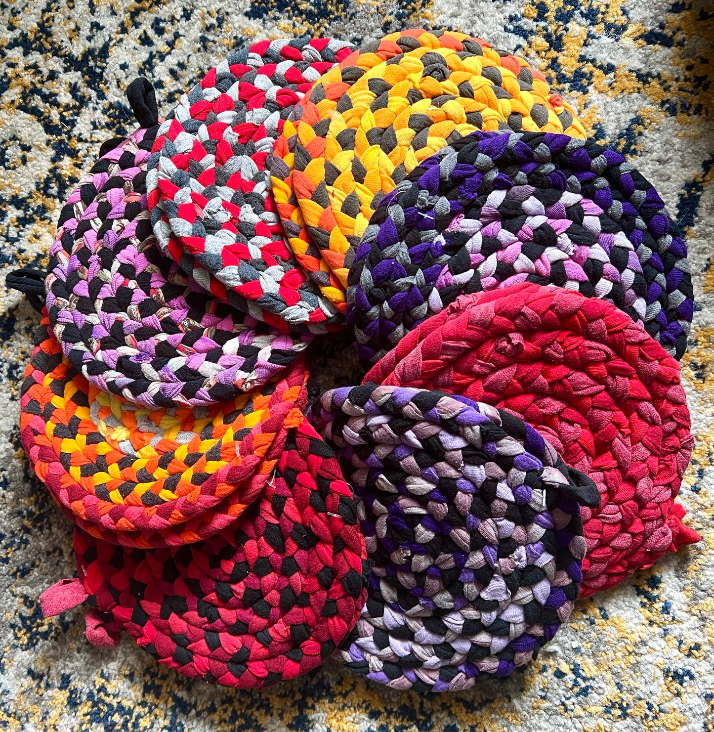 Colorful braided trivet potholders, upcycled from tshirt scraps on a textured surface