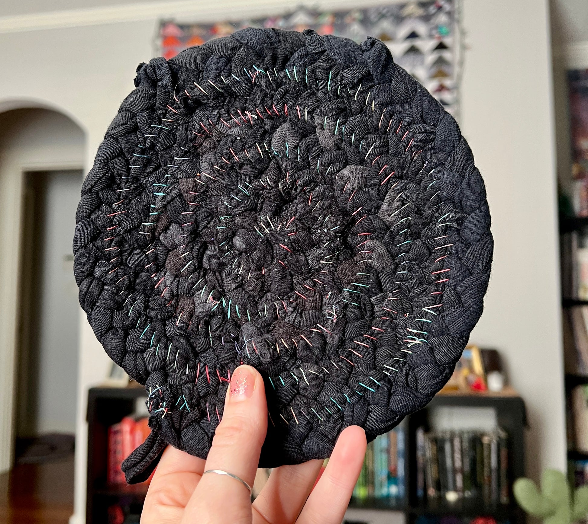 Trivet potholder single black, held up to show scale and texture of the back, where rainbow thread is handstitched