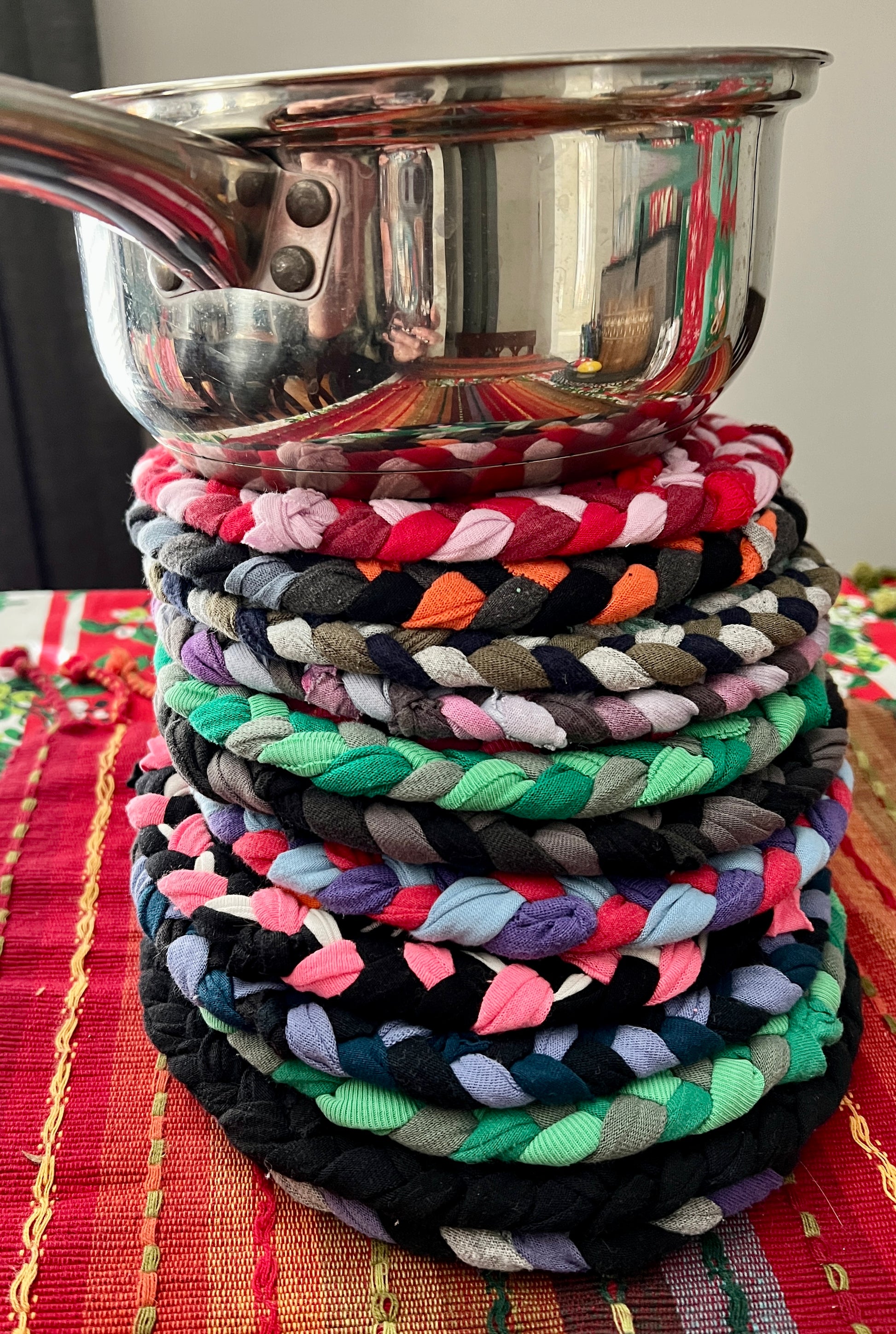 Trivet potholders group stacked under pan, showing off how beatuiful these hand braided trivets are, side view