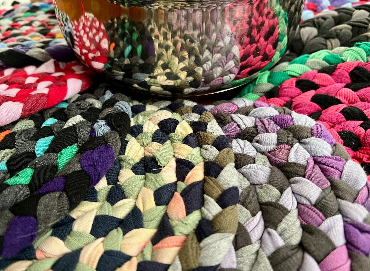 Trivet potholders group under pan, to show usage and scale. A reflection of the colorful trivets can be seen in the sauce pan