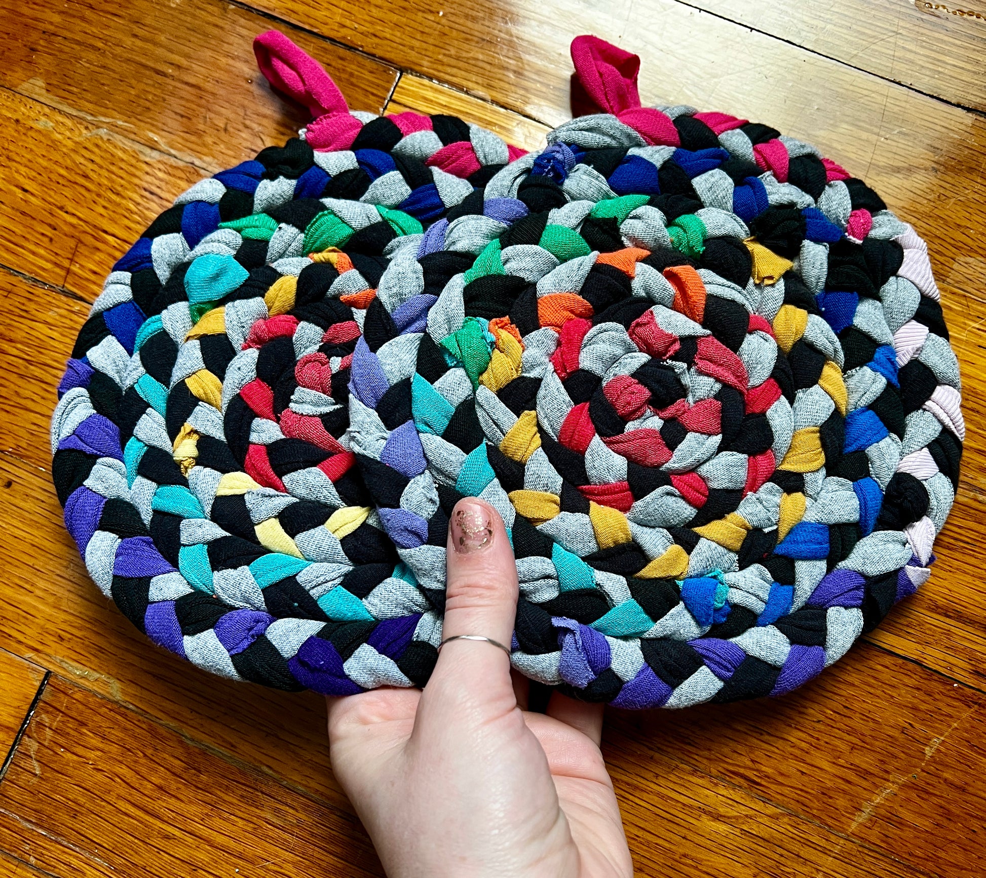 a set of two handbraided and handsewn potholders against a wood background, in hand for scale