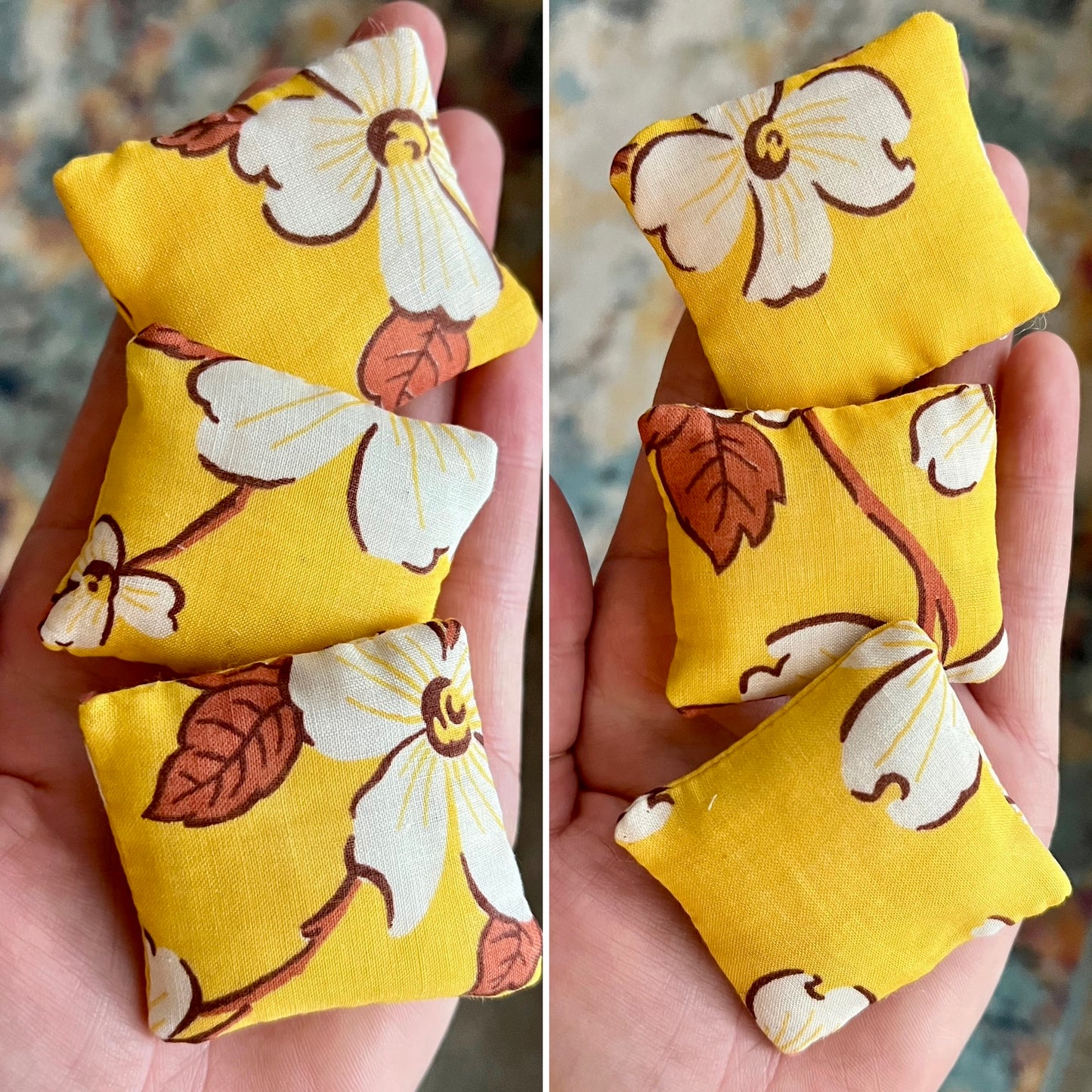 Three yellow fabric pillows with floral patterns held in a hand against a blurred background, showing front and back