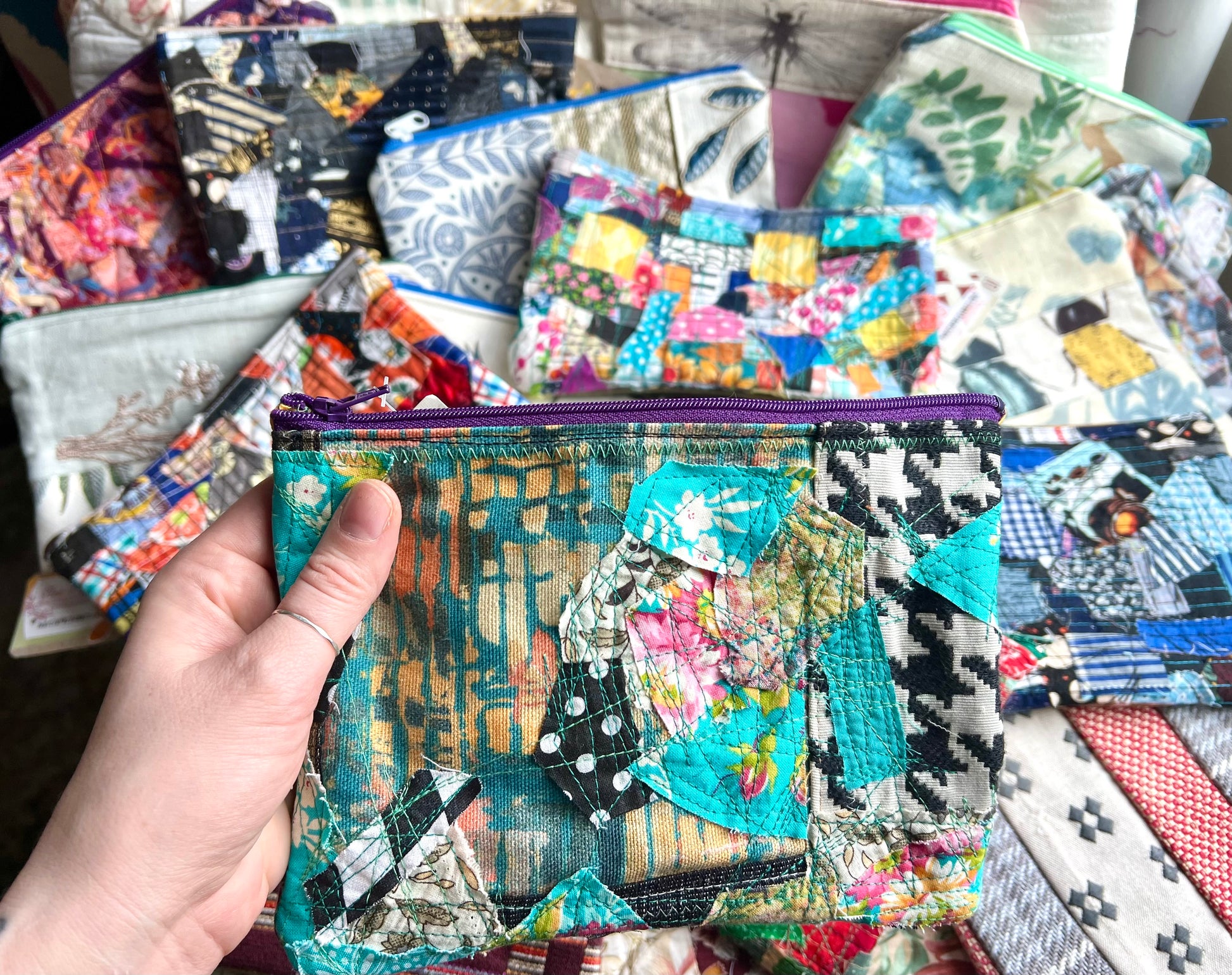 Hand holding a colorful patchwork pouch with more pouches in the background.