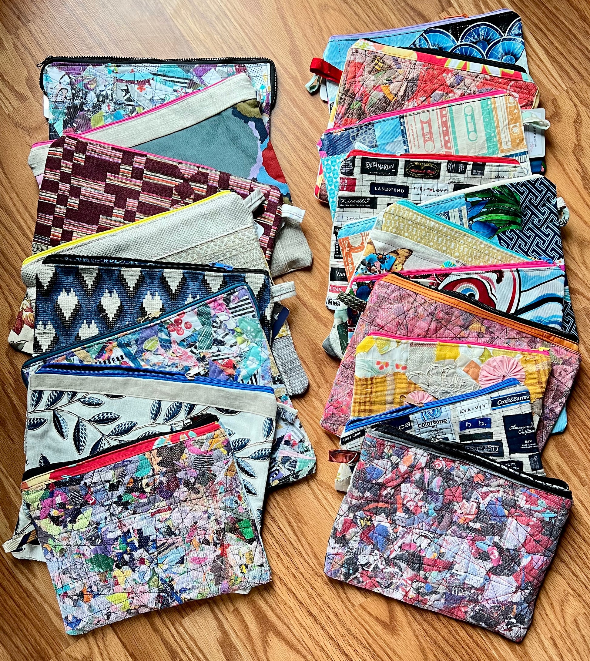 Two stacks of colorful zippered pouches with various printed and patterned fabrics, displayed on a wooden surface.