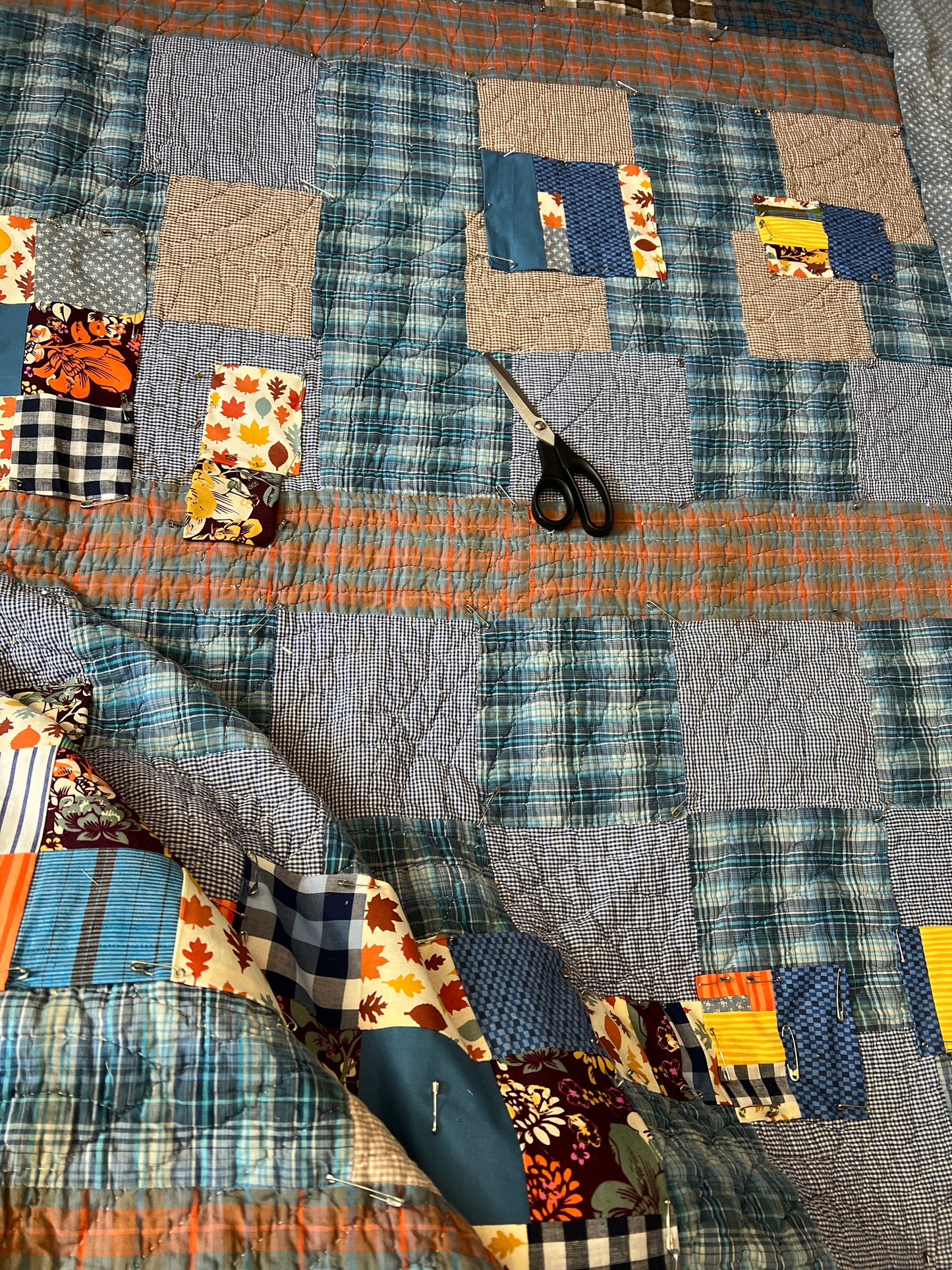 autumn blues quilt leaves closeup in progress, with scissors on top of quilt, and safety pines holding some squares in place