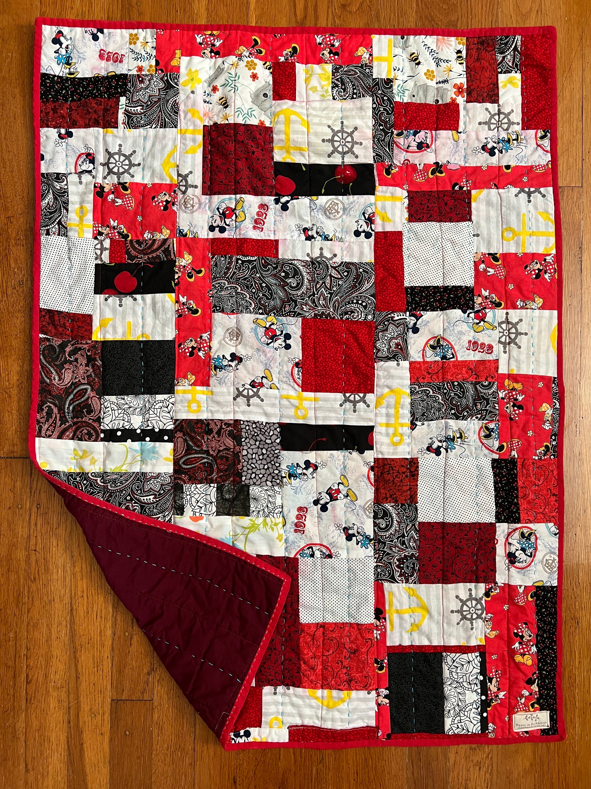 aerial view of a baby quilt, against a wood background, one corner upturned to show the back