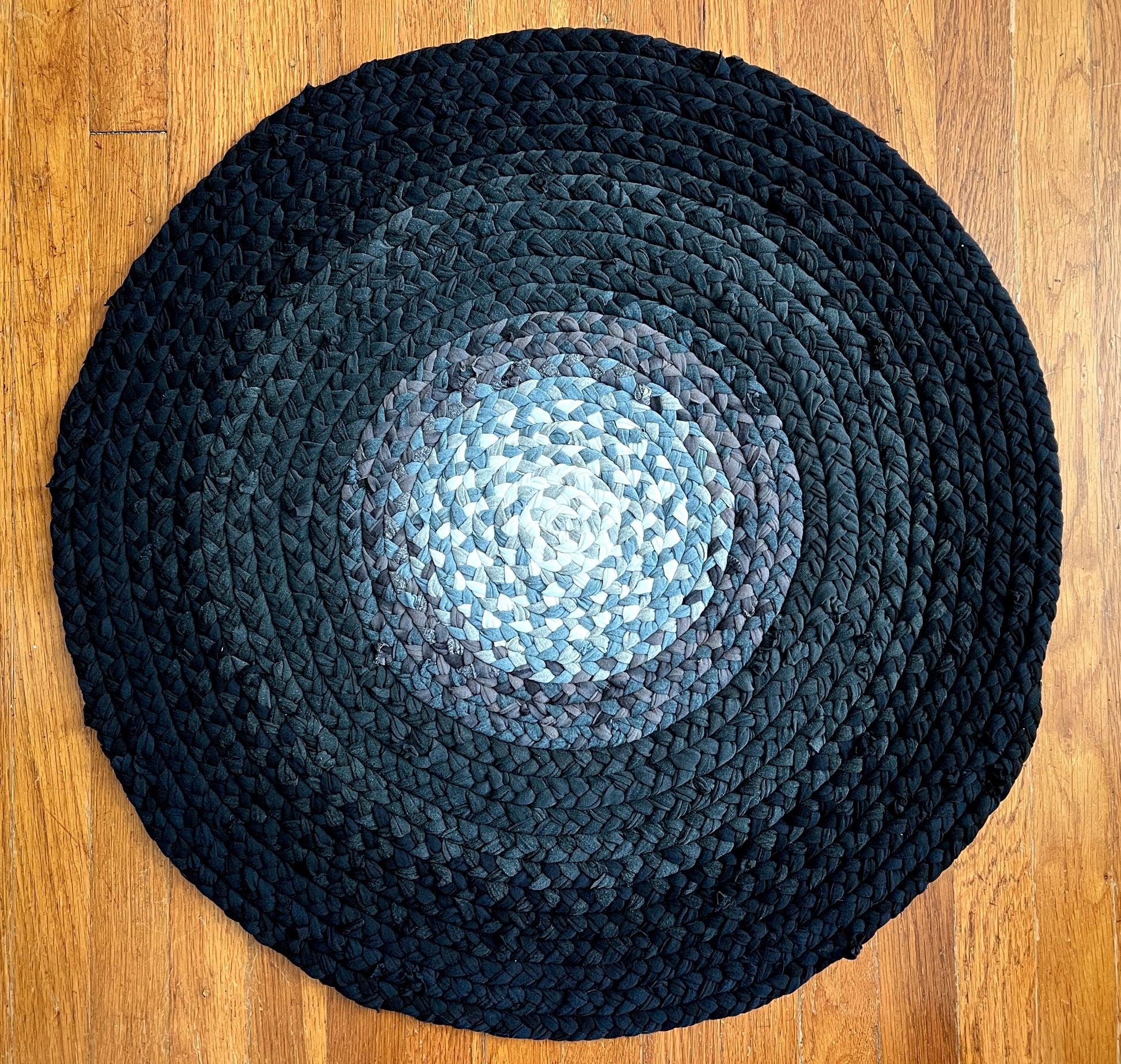 aerial view of black grey ombre handbraided rug, on a wood floor background