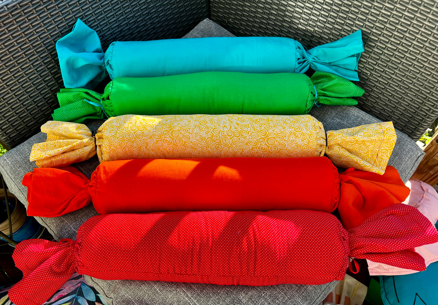 a group of candy wrap bolster pillows, in a row, rainbow order