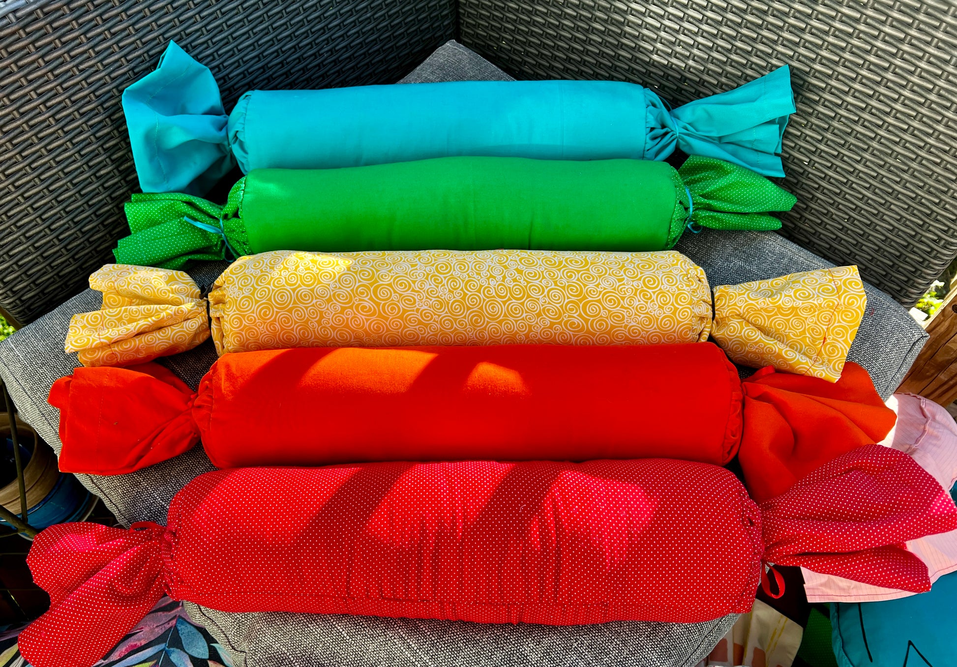 a group of candy wrap bolster pillows, in a row, rainbow order