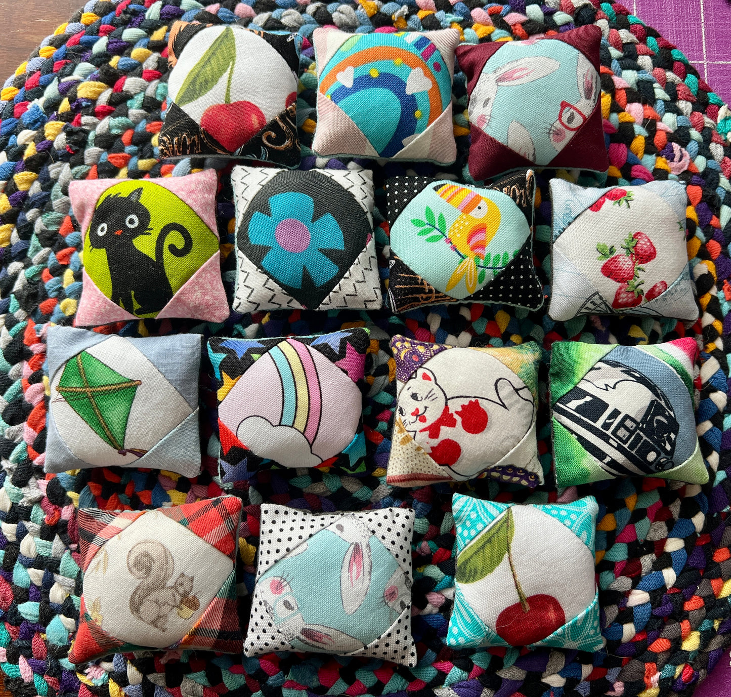 Collection of small fabric pillows with various designs on a colorful braided rug.
