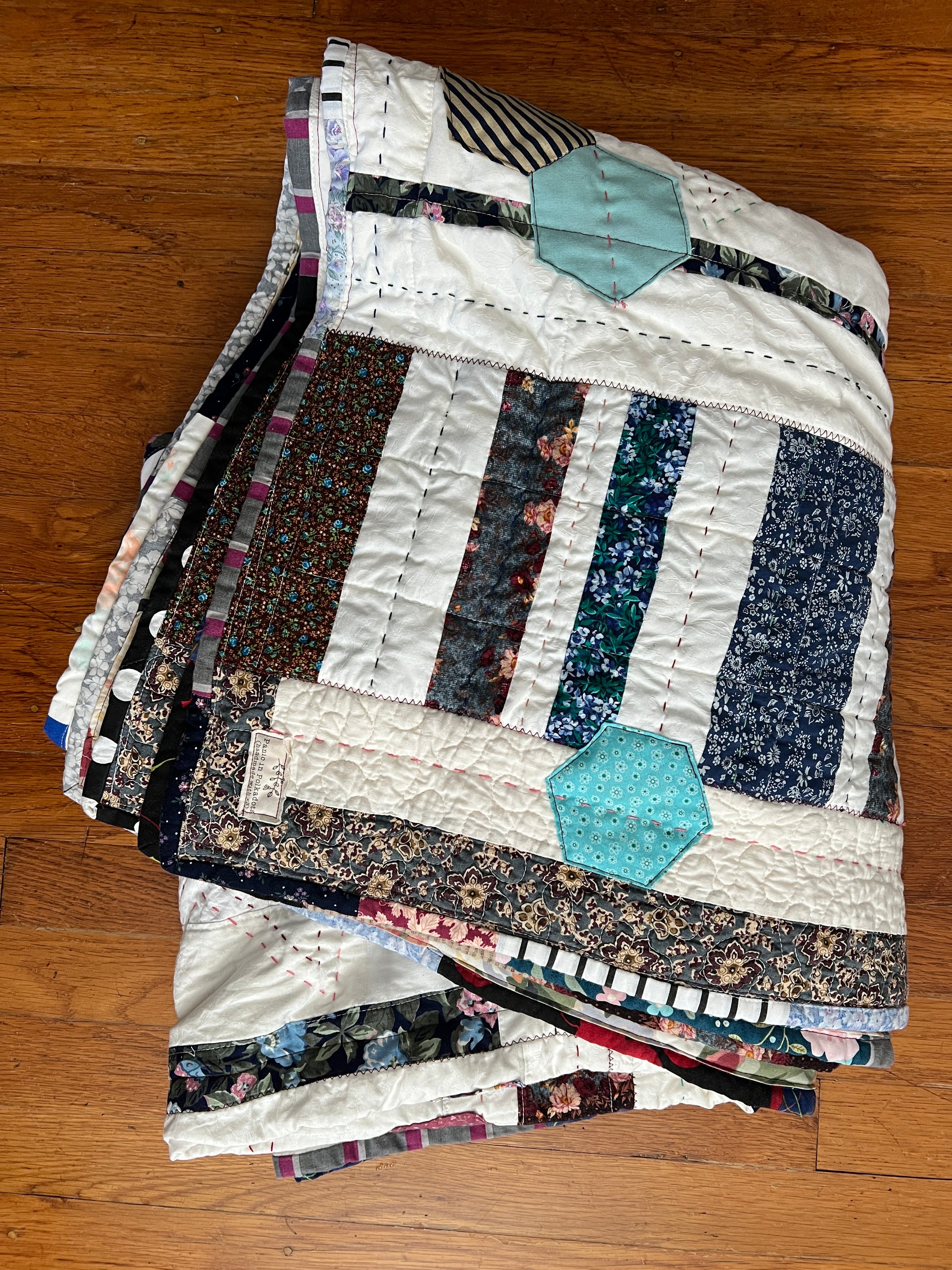 A quilt with eight point stars and quilted hexies, folded with the top corner showing off a label that reads Panic in Polkadots (handmade with love)