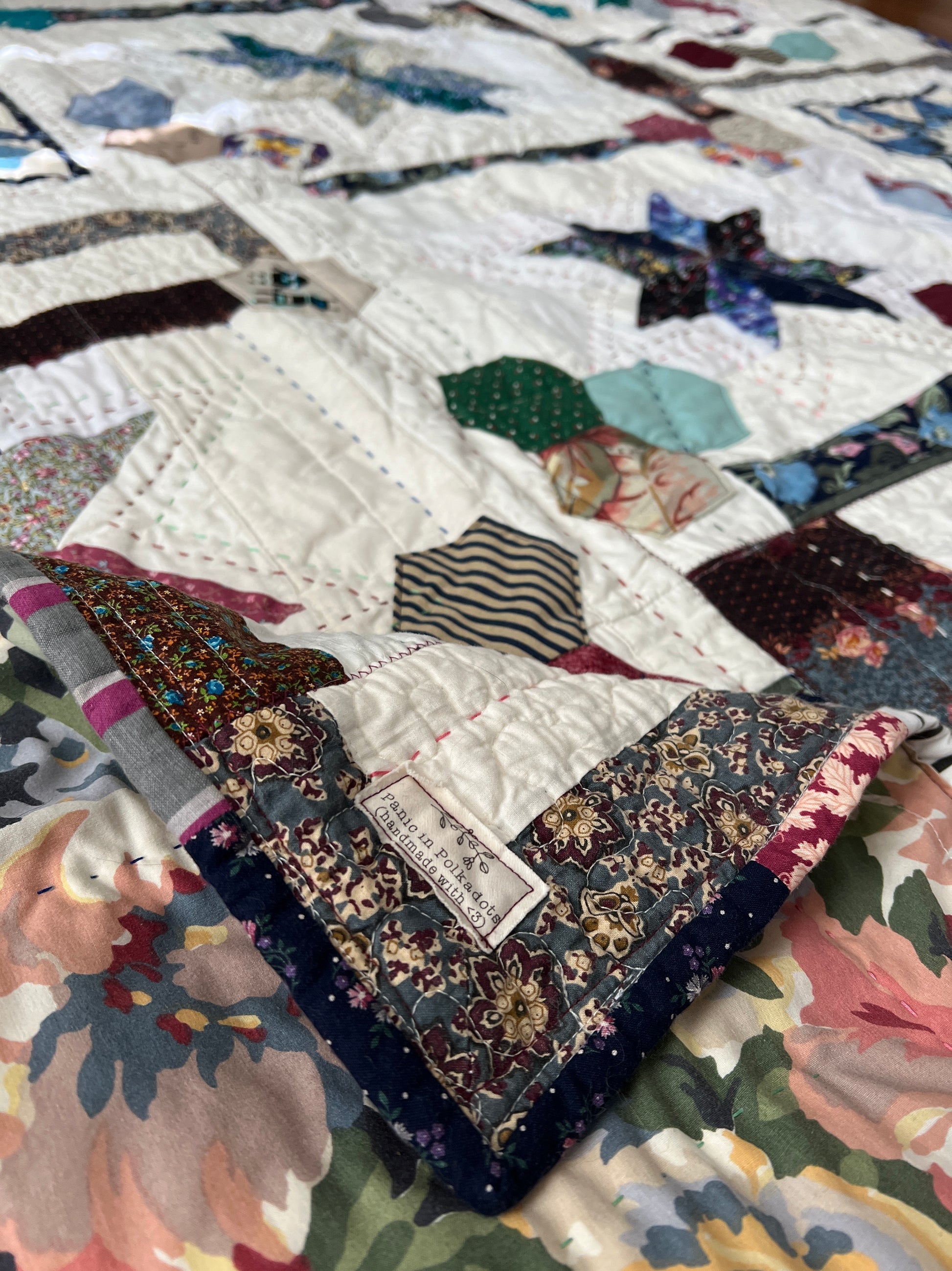 A quilt with eight point stars and quilted hexies, corner folded over twice to show Panic label in front, and top of the quilt in background