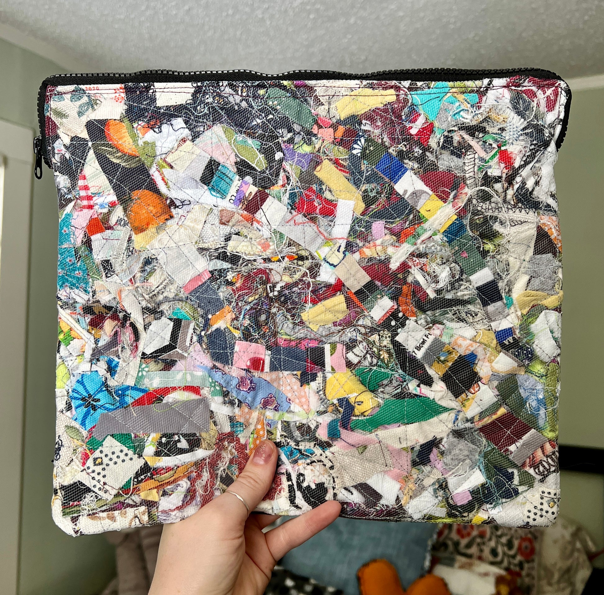 ipad case, held up for scale, created from fabric scraps under a tulle layer, zipper closure, padded, with inside pocket