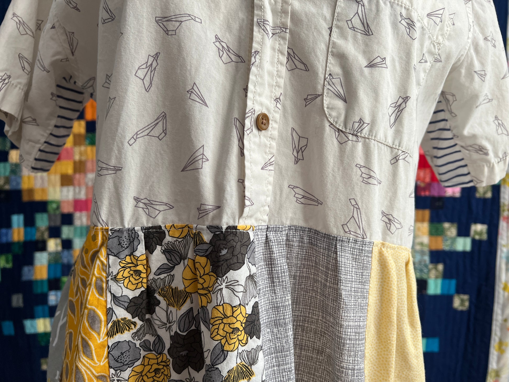 closeup detail of patchwork dress in yellows and greys, with a paper airplanes button up shirt