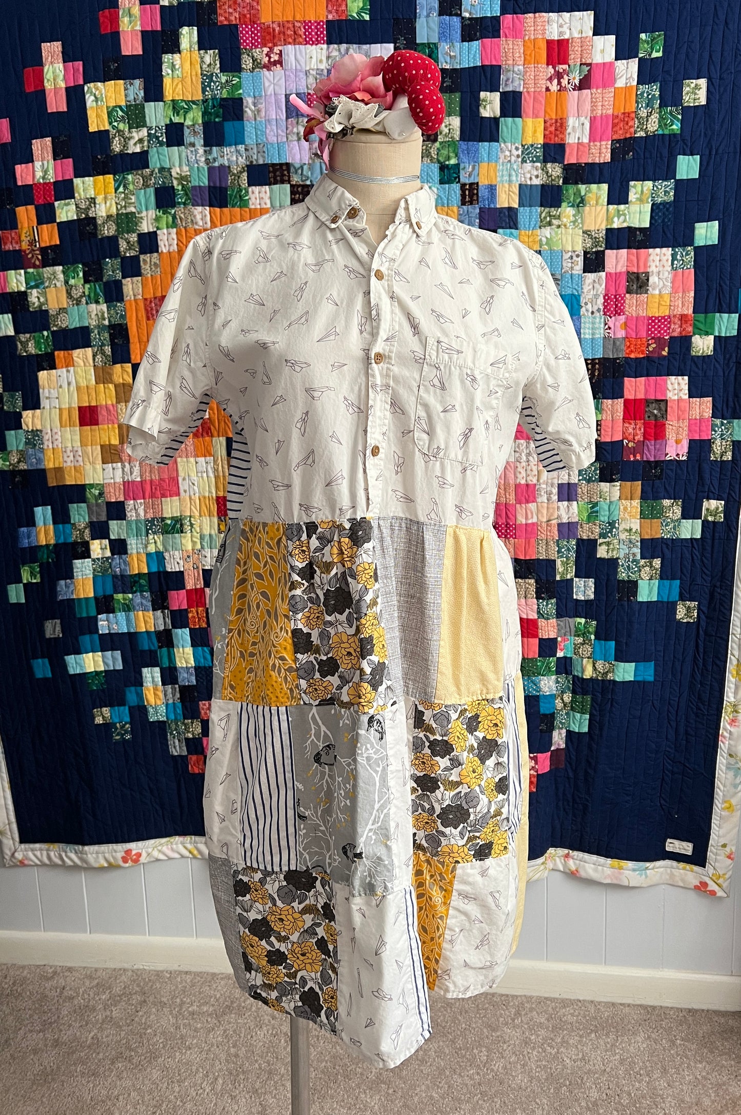 A shirtdress in mostly whites, yellows, and greys. Top is button up, bottom is a patchwork skirt. 